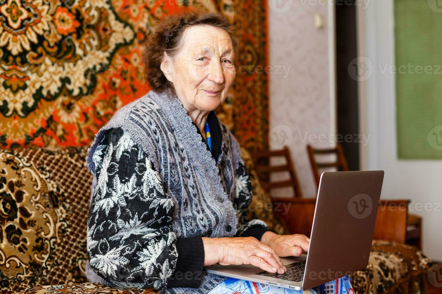 Old woman working on laptop computer at home, Grandma using notebook and searching on internet site photo