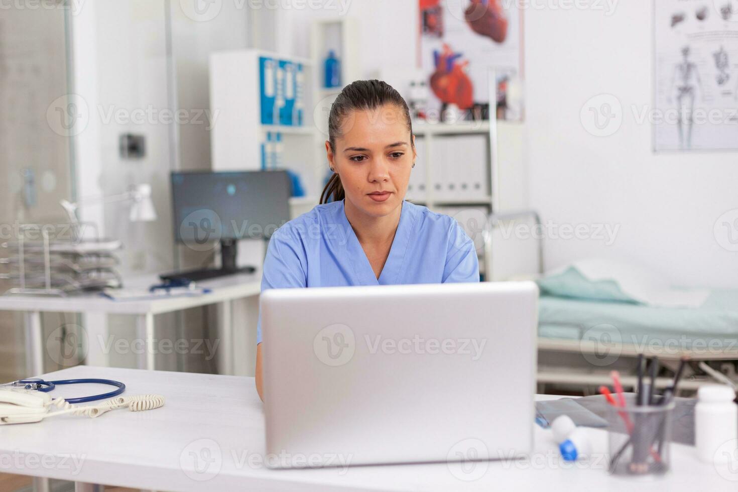 Medical practitioner typing patient health report on laptop in hospital office. Health care staff sitting at desk using computer in modern clinic looking at monitor, medicine. photo