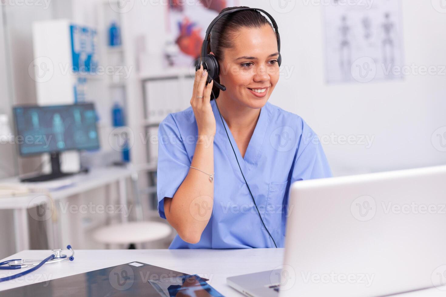 Medical staff talking with patient about prescription wearing headset with microphone in hospital office. Health care physician sitting at desk using computer in modern clinic looking at monitor. photo