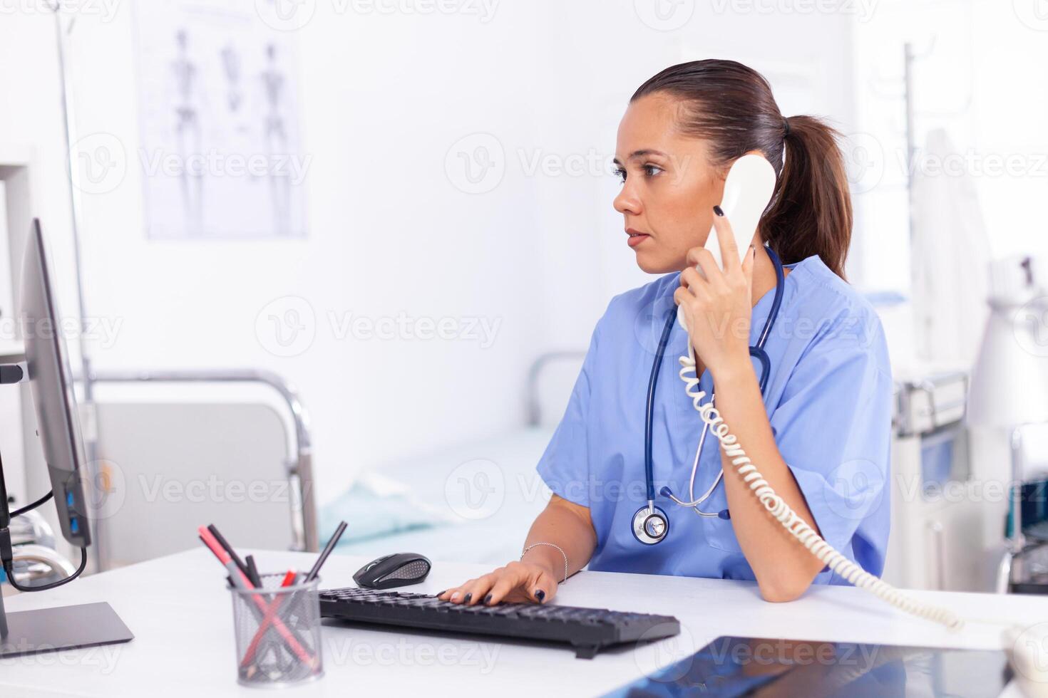 Medical nurse talking with patient on the phone about diagnosis. Health care physician sitting at desk using computer in modern clinic looking at monitor. photo