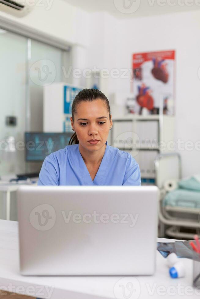 Medical practitioner typing patient health report on laptop in hospital office. Health care staff sitting at desk using computer in modern clinic looking at monitor, medicine. photo