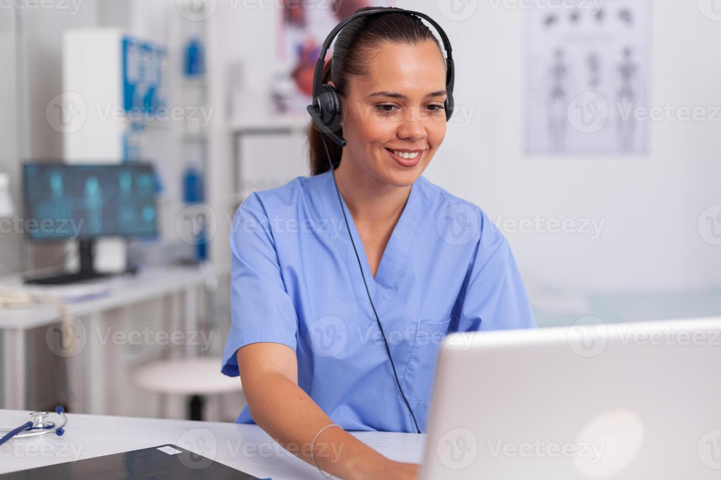 Medical staff talking with patient about prescription wearing headset with microphone in hospital office. Health care physician sitting at desk using computer in modern clinic looking at monitor. photo