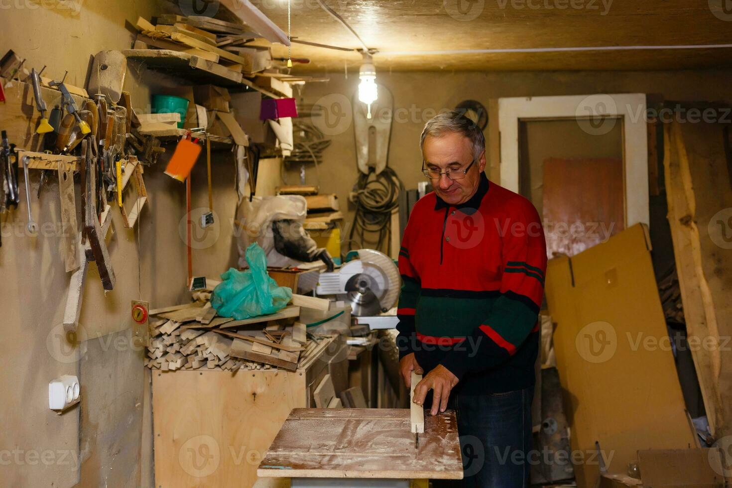 Satisfied cheerful joyful smiling woodmaster is standing near desktop in his workshop, workstation photo