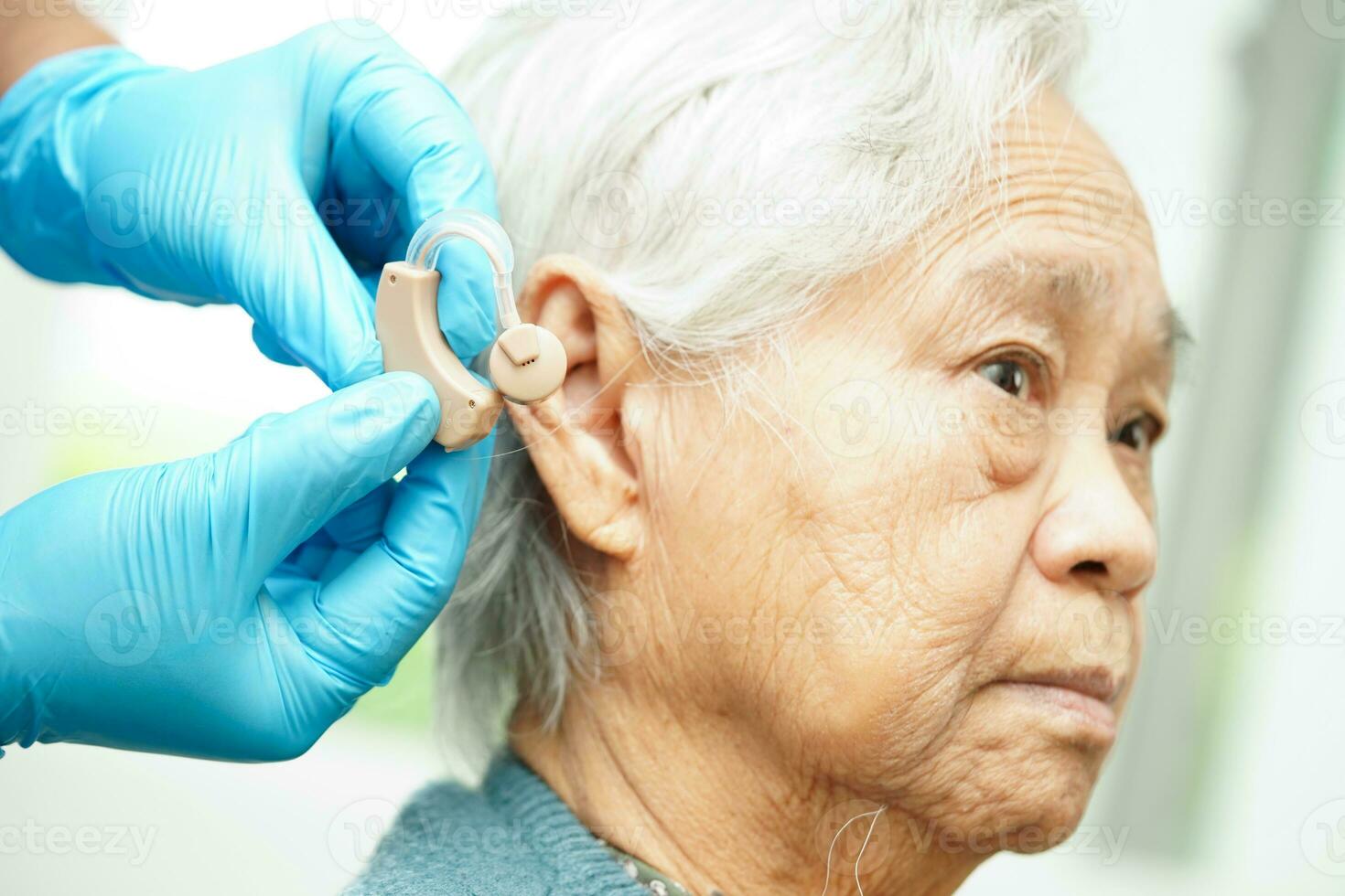 Doctor install hearing aid on senior patient ear to reduce hearing loss problem. photo