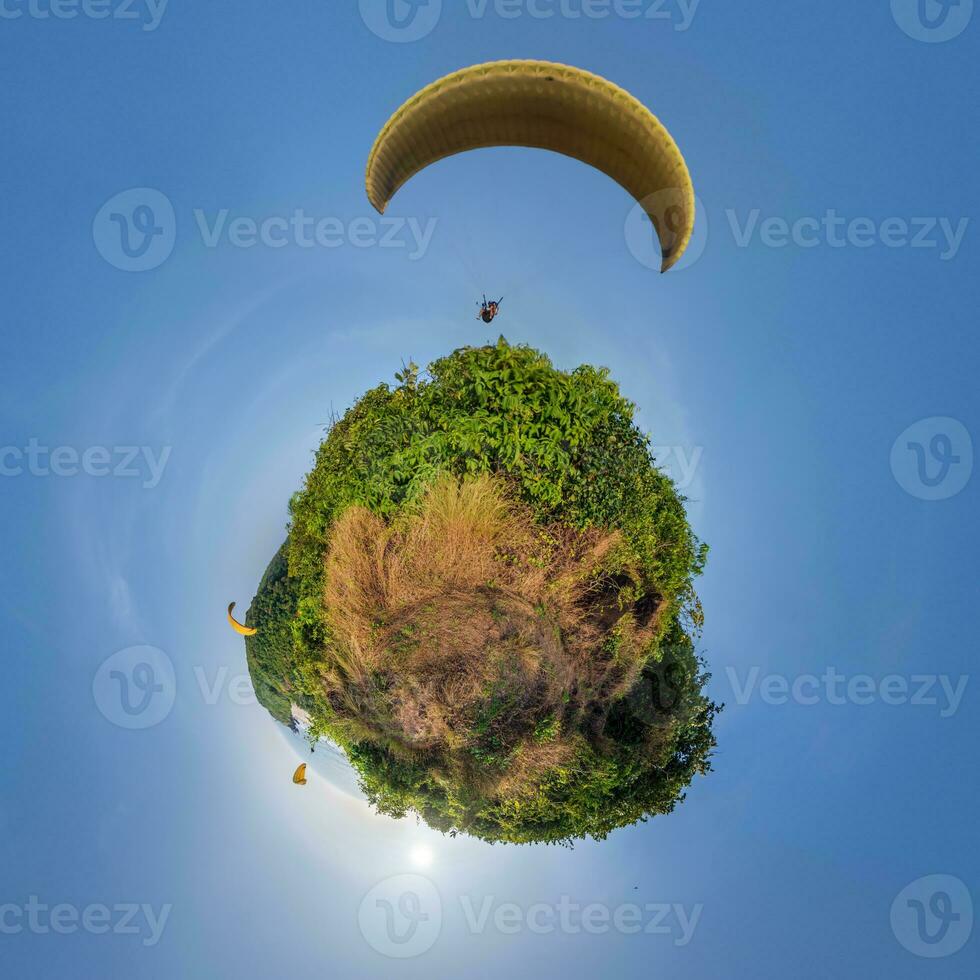 green grass little planet in blue sky with yellow paragliding parachute photo