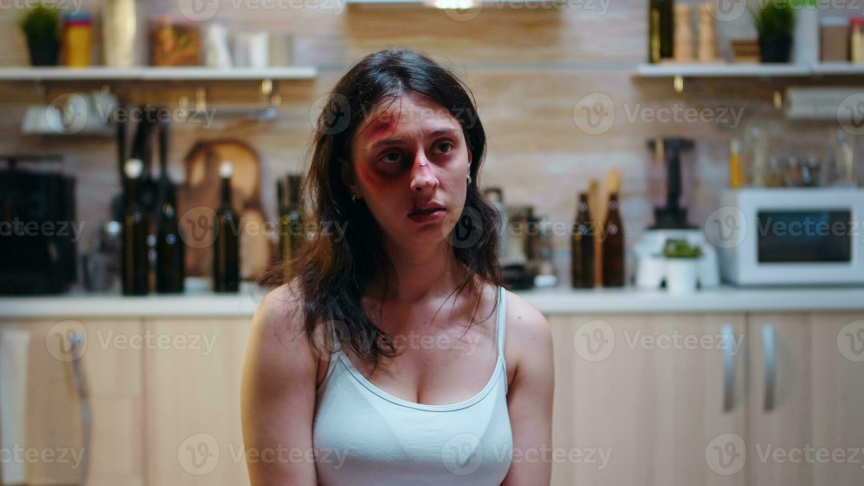 Abused wife having despair face sitting in the kitchen. Traumatised hit terrified beaten wife covered in bruises suffering injury from alcoholic aggression brutal drunk man. photo