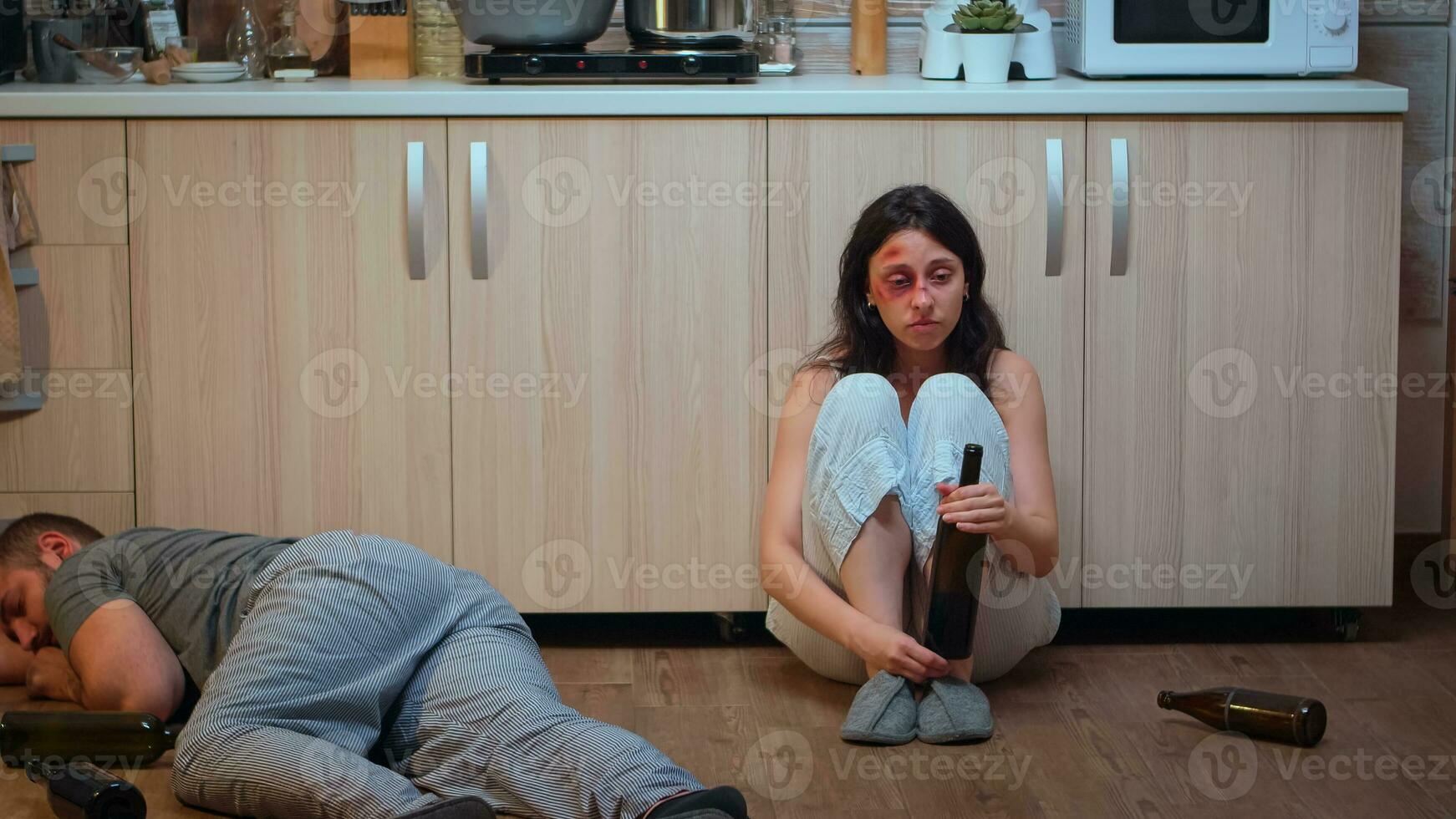 Wife drinking alcohol near drunk husband looking desolated at him. Traumatised abused terrified beaten woman covered in bruises suffering injury from alcoholic aggression brutal violent man. photo