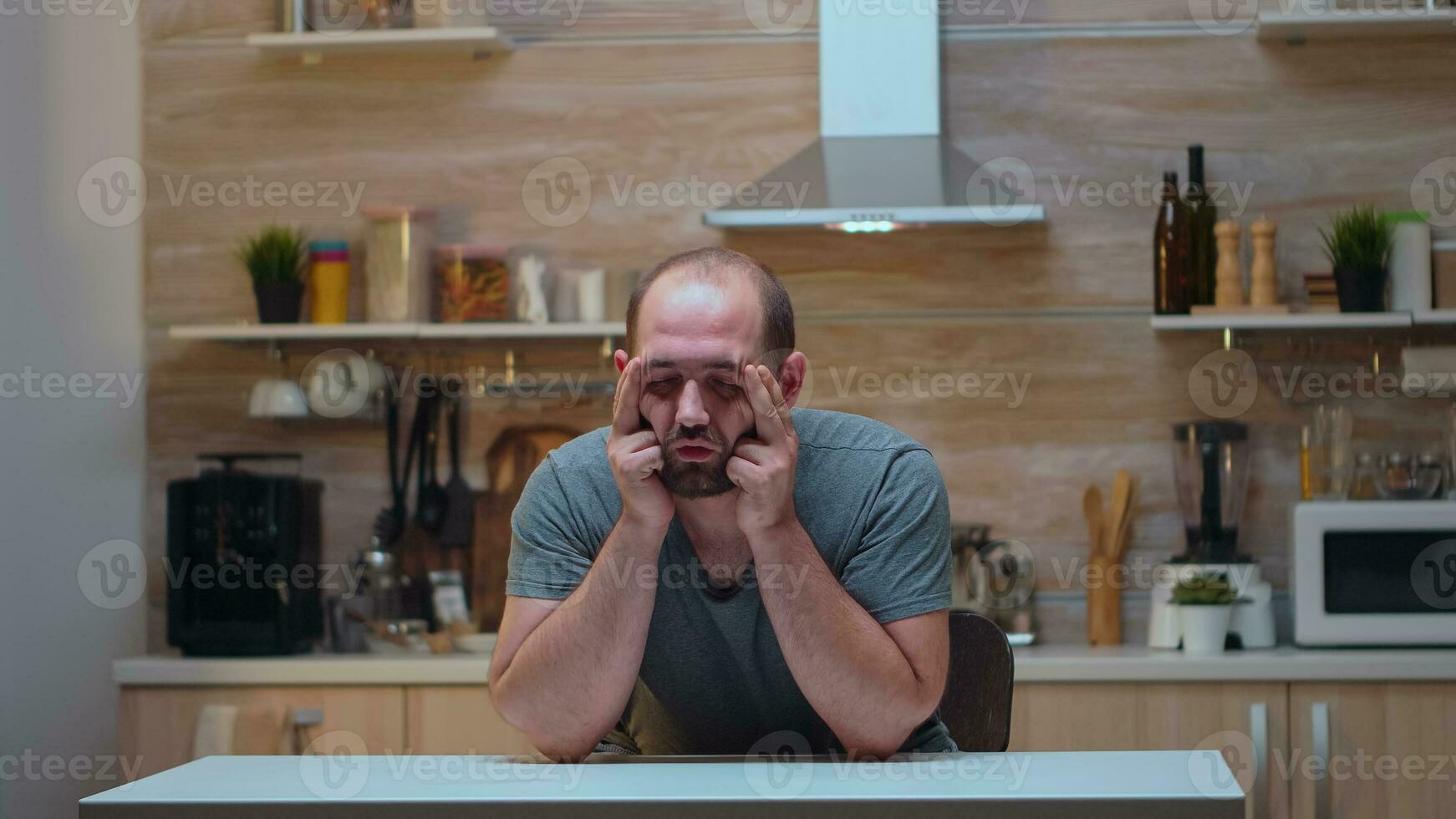 Man with headaches sitting in the kitchen massaging his temples. Stressed tired worried unwell person suffering of migraine, depression, disease and anxiety feeling exhausted with dizziness symptoms. photo
