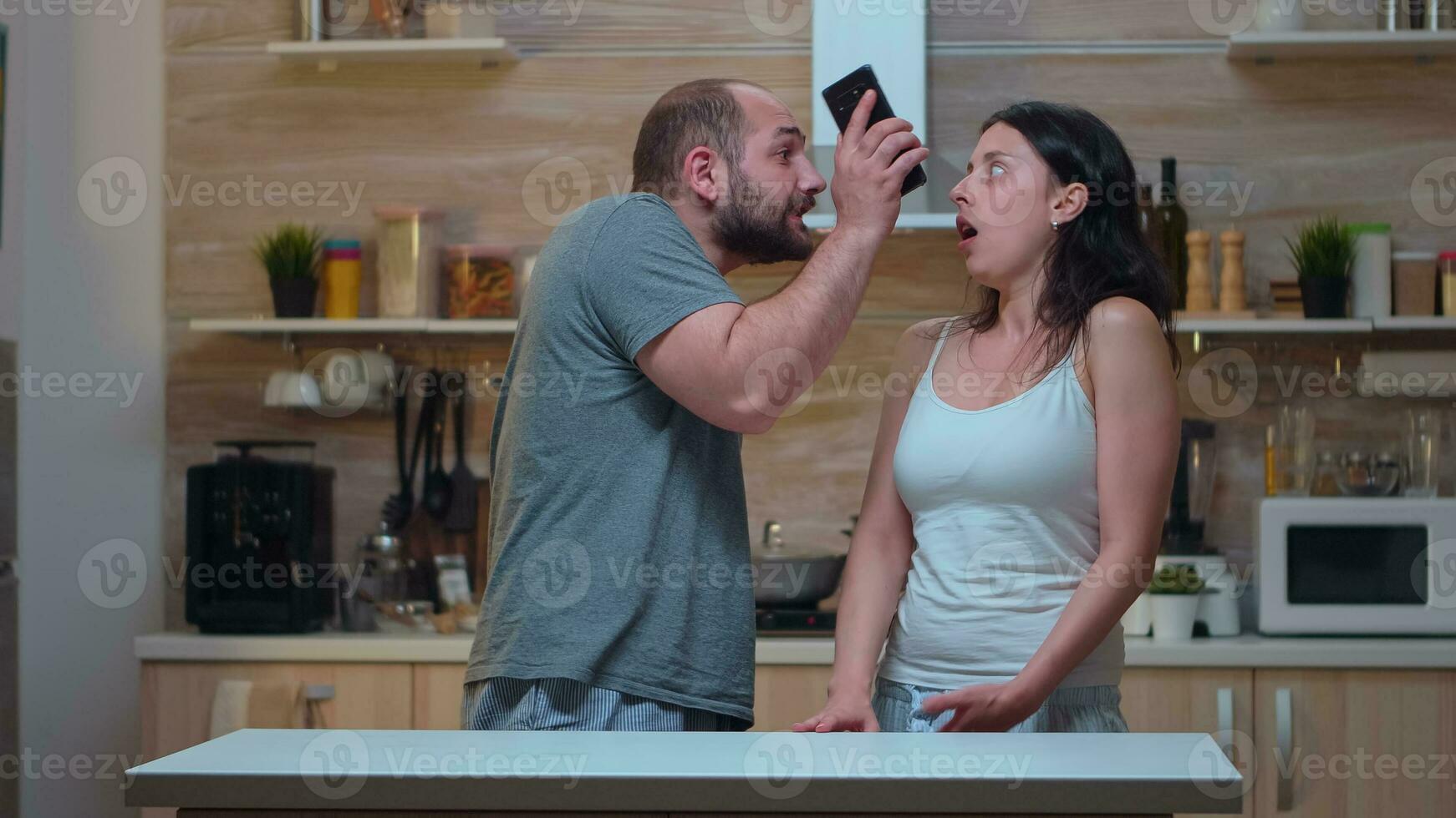 enojado hombre Gritando a infiel esposa en el cocina. celoso compañero engañado frustrado ofendido irritado acusando mujer de infidelidad discutiendo su con mensajes en teléfono inteligente gritando desesperado foto