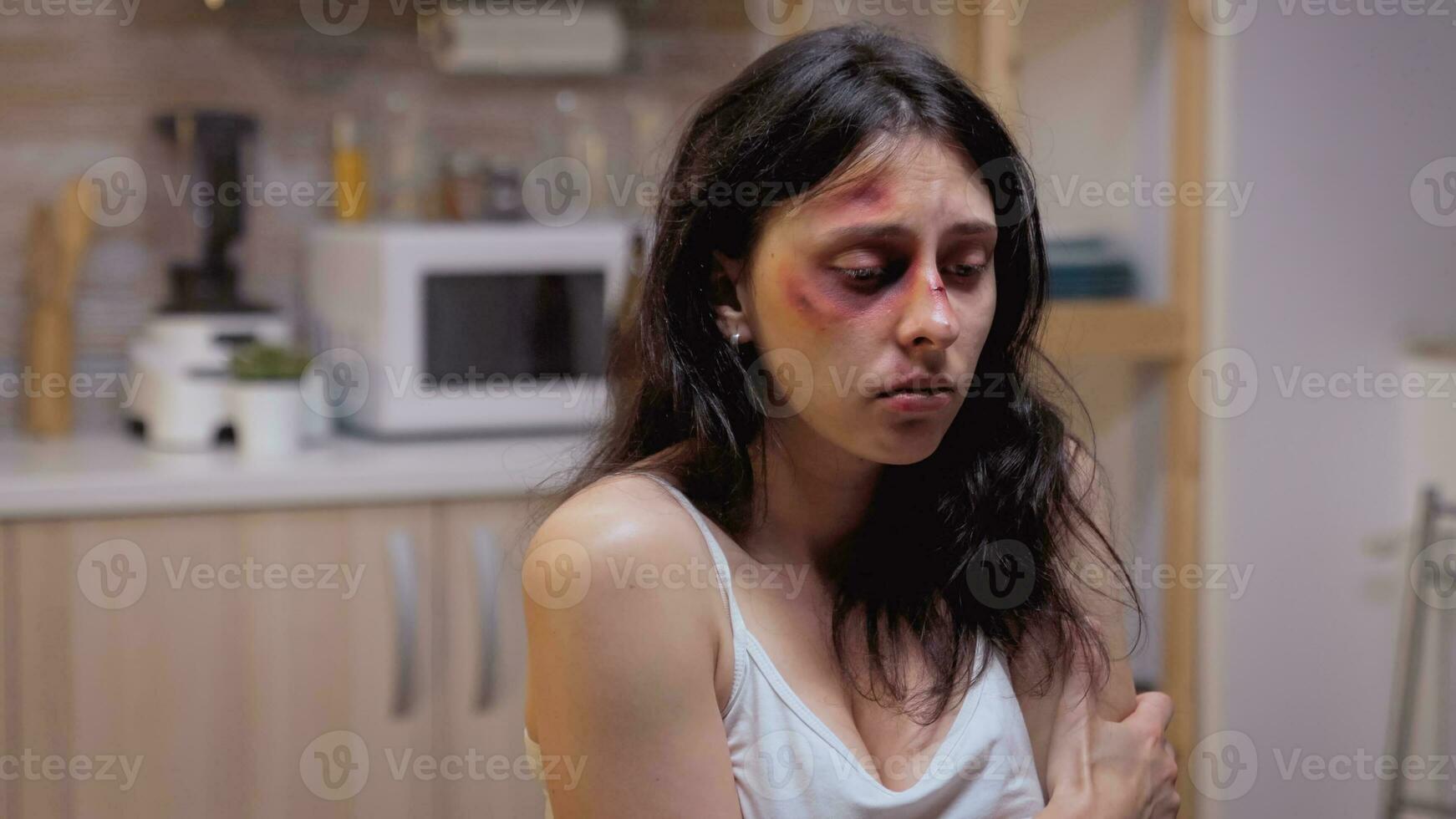 Beaten woman siting on the chair pushed by violent husband. Traumatised abused terrified beaten wife covered in bruises suffering injury from alcoholic aggressive brutal drunk man. photo