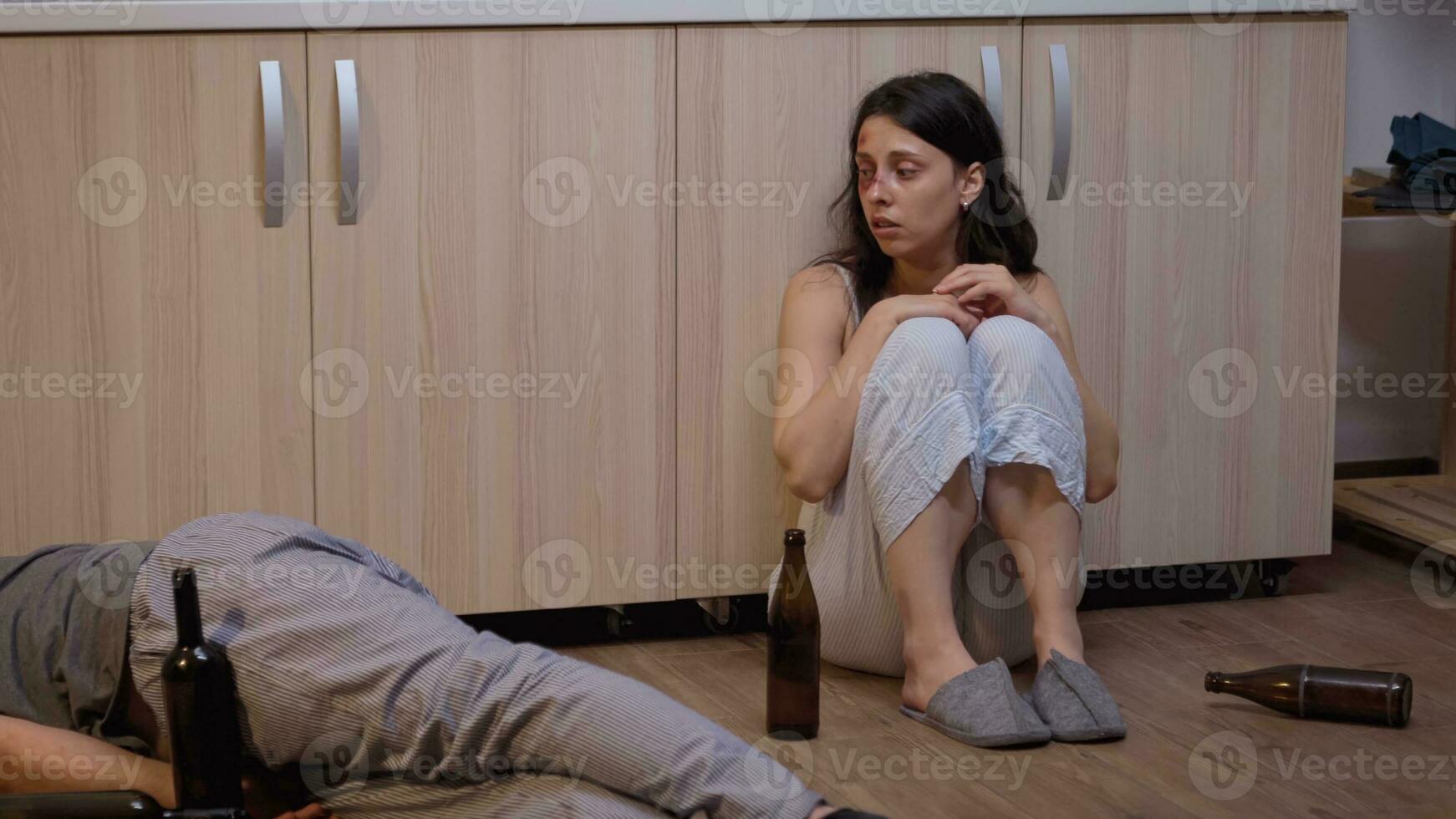 Abused wife calling for help when husband is lying on the floor. Violent aggressive man abusing injuring terrified helpless, vulnerable, afraid, beaten and panicked wife living in terror and pressure. photo