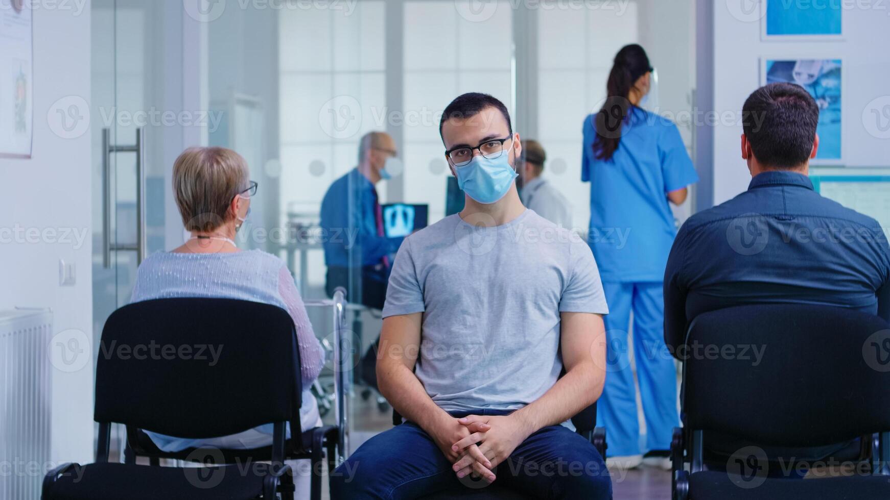 Young man with face mask against coronavirus looking at camera in hospital waiting area. Senior woman with walking frame waiting for consultation in clinic. photo