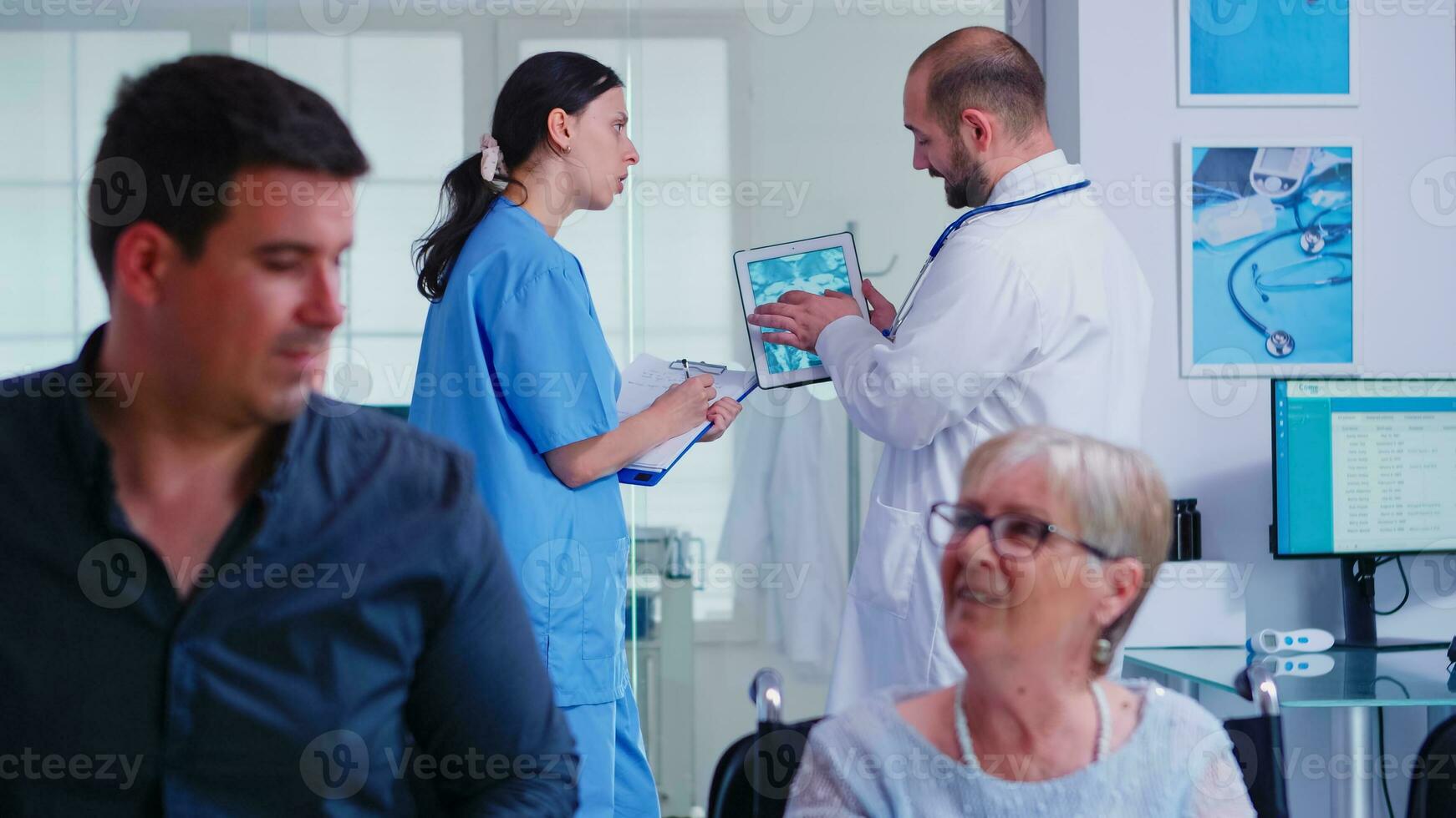 Doctor pointing at tablet pc with patient xray while discussing with nurse in hospital hallway. Doctor wearing white coat and stethoscope. Health care system medical diagnosis disease teamwork photo