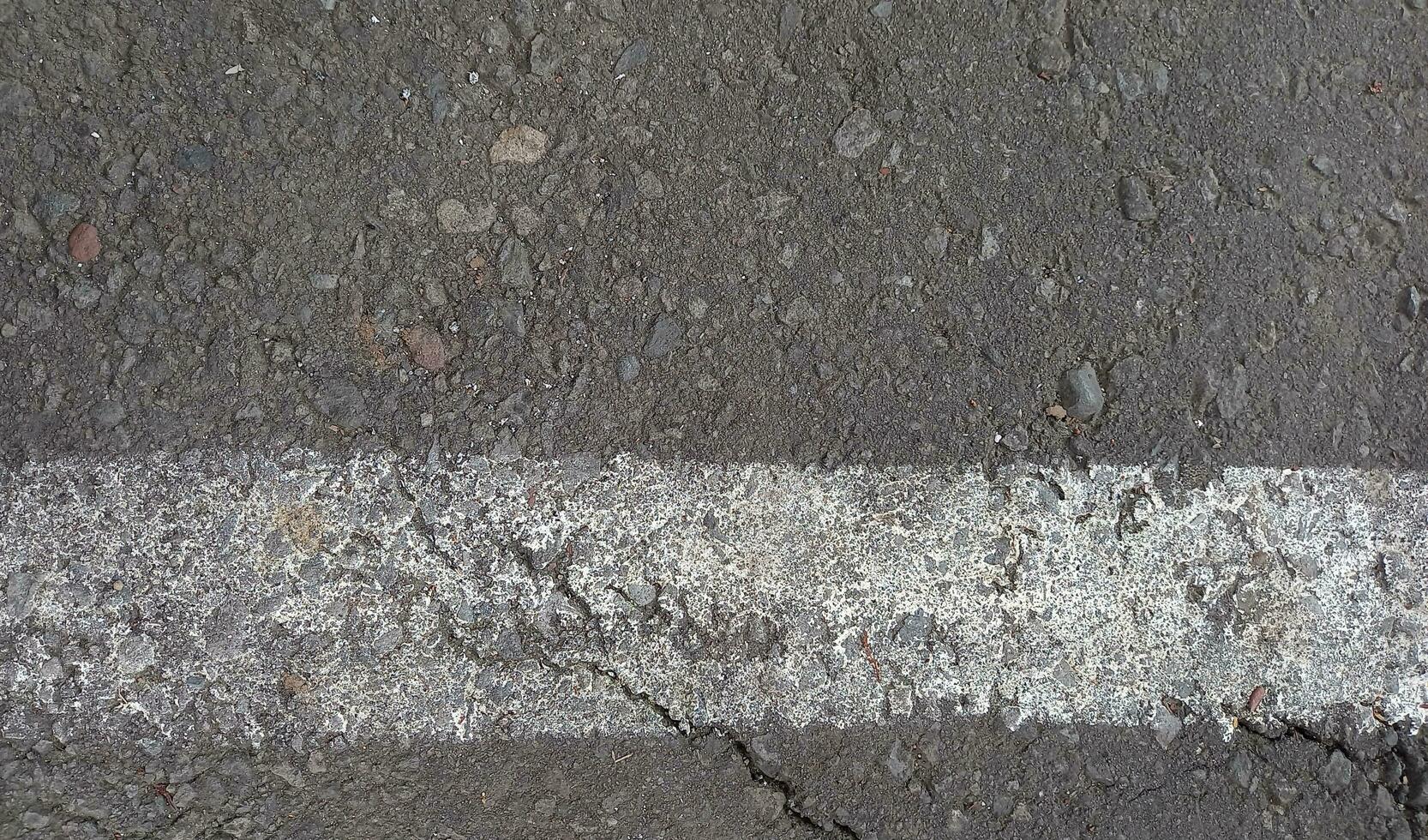 gris asfalto con blanco líneas. áspero cemento la carretera superficie. agrietado asfalto la carretera antecedentes. foto