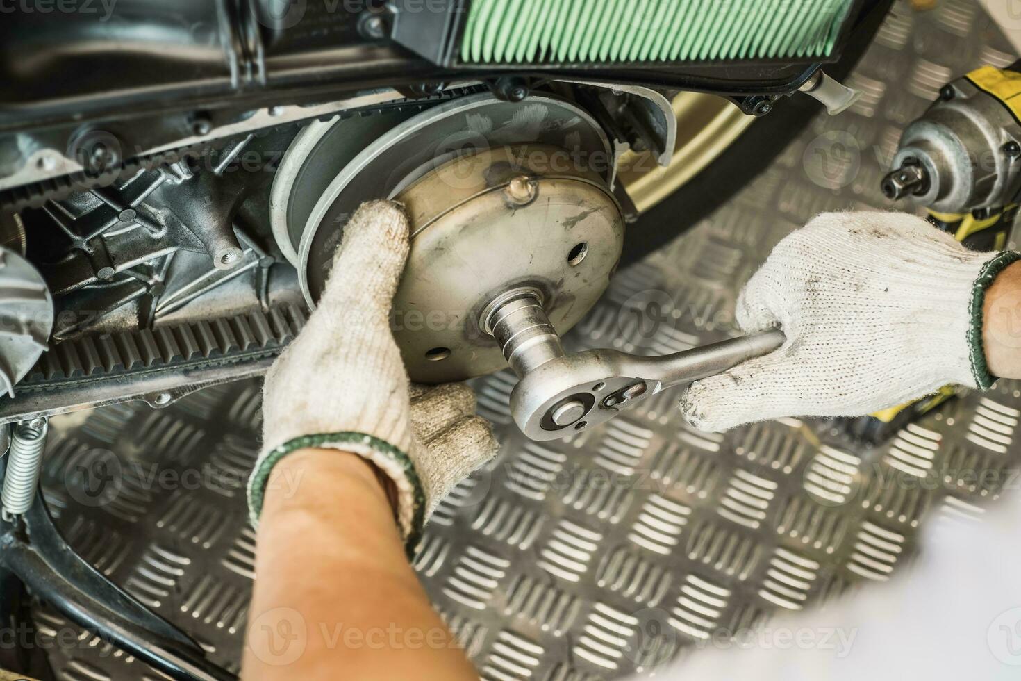 Mechanic using wrench and socket to Remove auto Transmission system or Rear Clutch Pulley of scooter Motorcycles,working in garage maintenance, repair motorcycle concept .selective focus photo