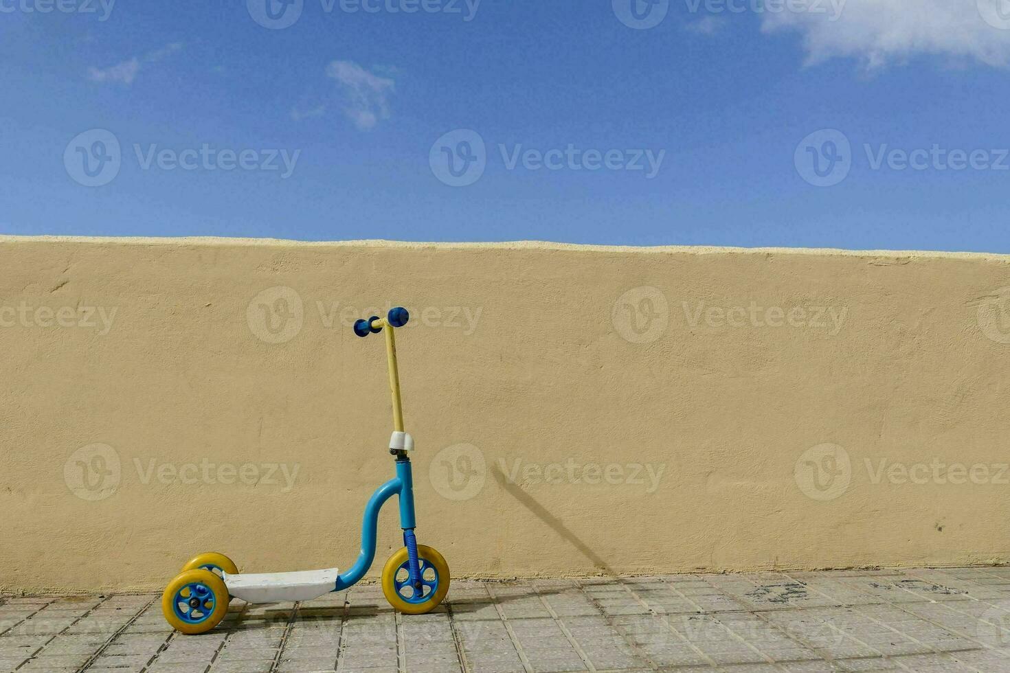 a small blue scooter against a yellow wall photo