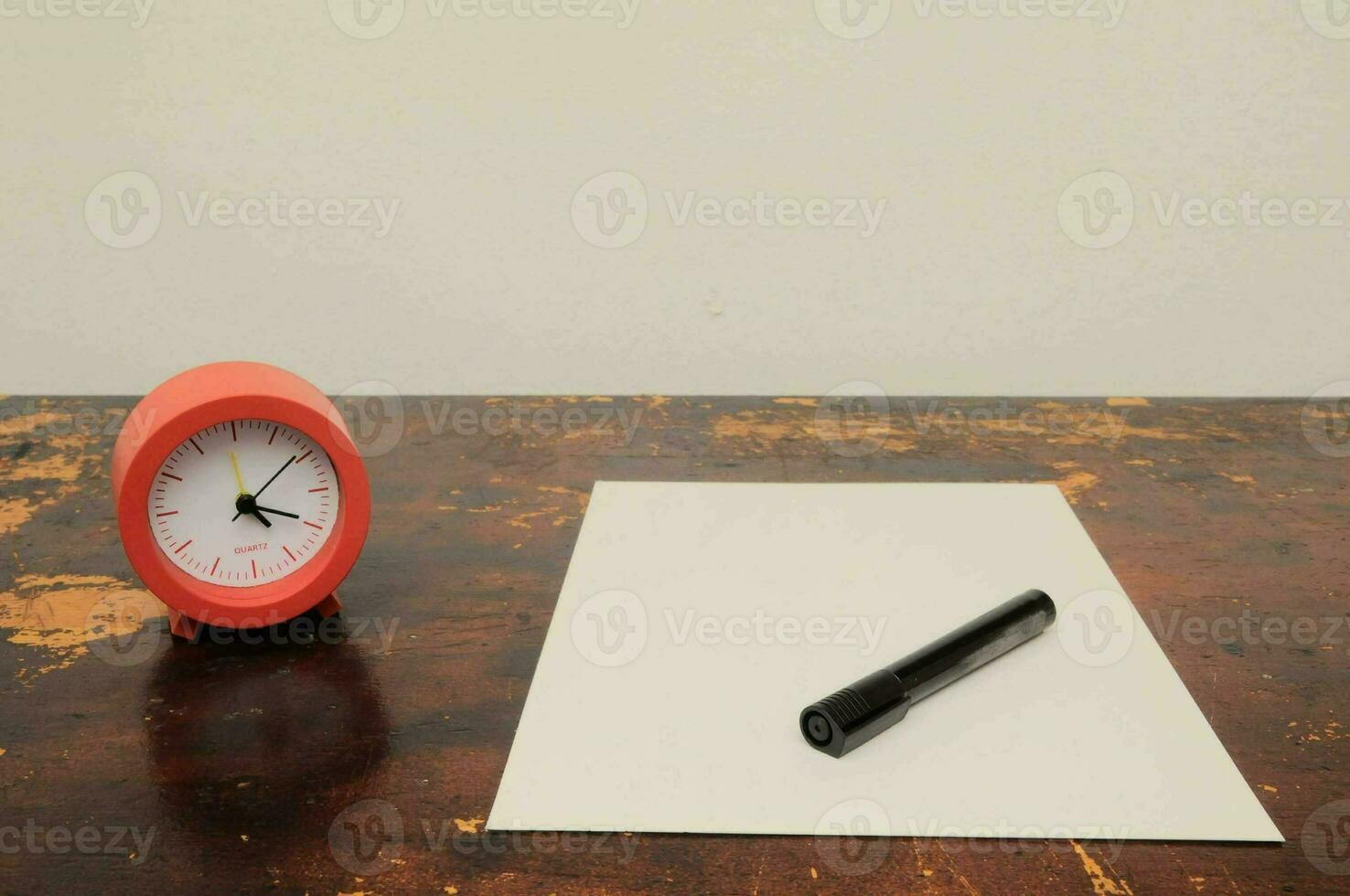 a red alarm clock and a white sheet of paper on a table photo