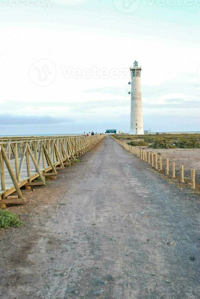 a lighthouse on a dirt road near the ocean photo