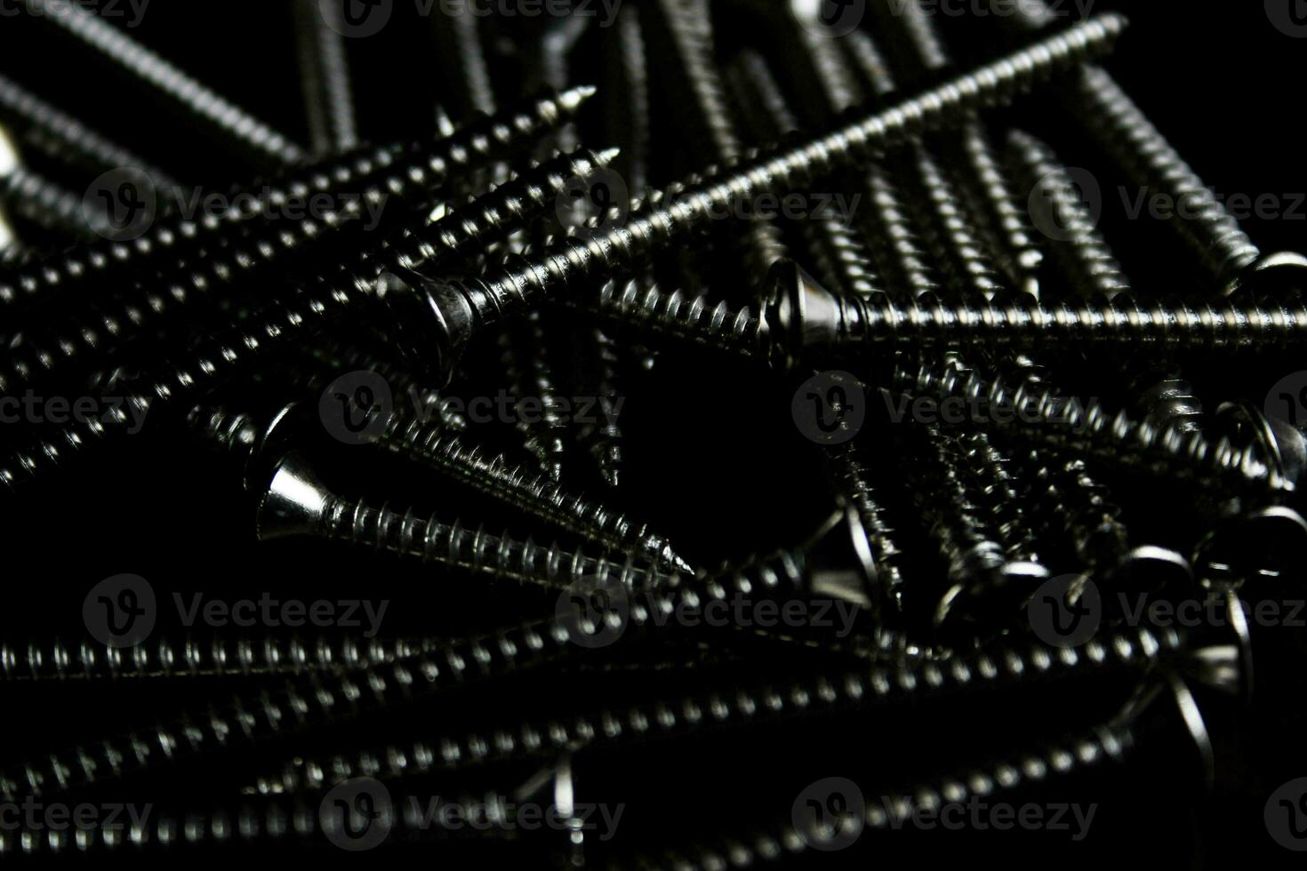 The screws are placed on a black wooden table with lighting from the side. photo
