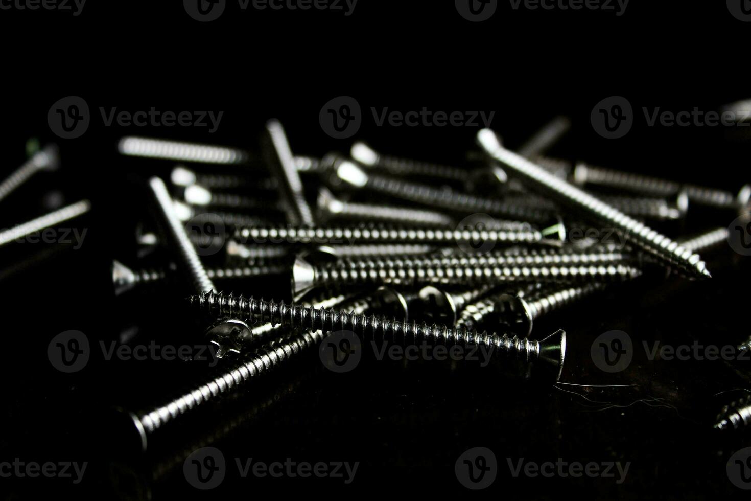 The screws are placed on a black wooden table with lighting from the side. photo