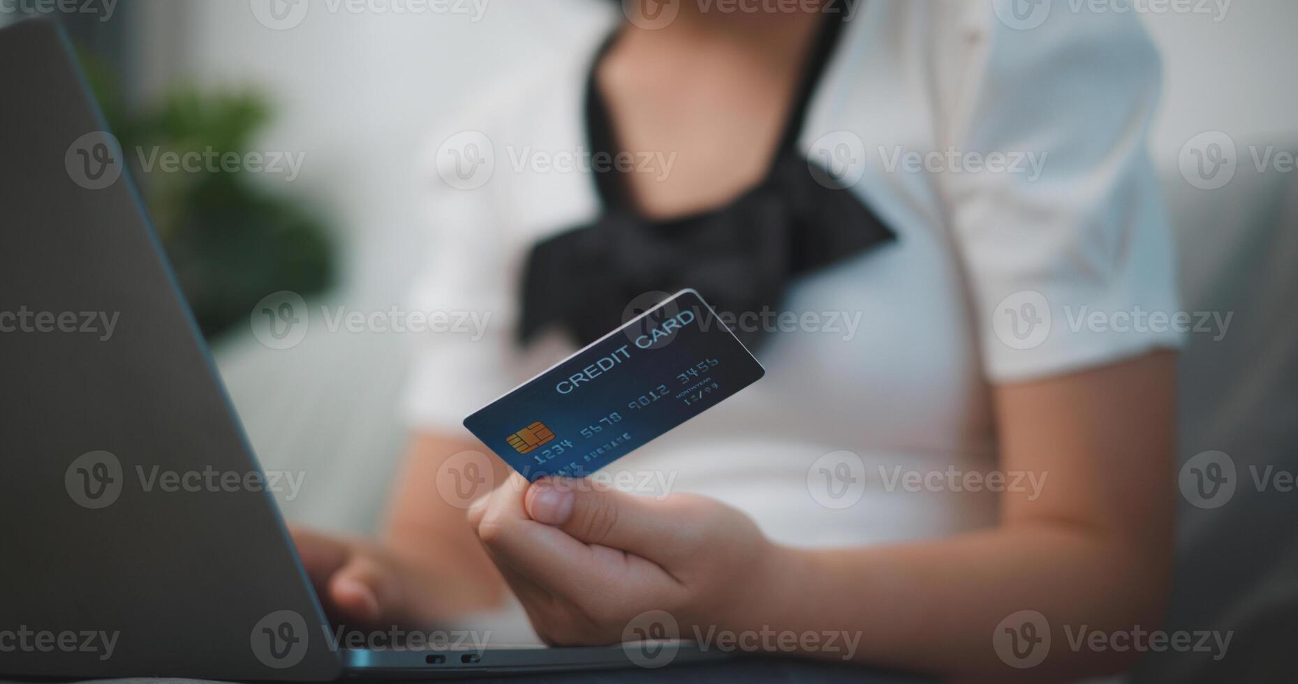 retrato de joven asiático mujer sentado en sofá en vivo habitación, hace en línea bancario pagos mediante el Internet desde banco tarjeta en portátil, compras en línea con crédito tarjeta. foto