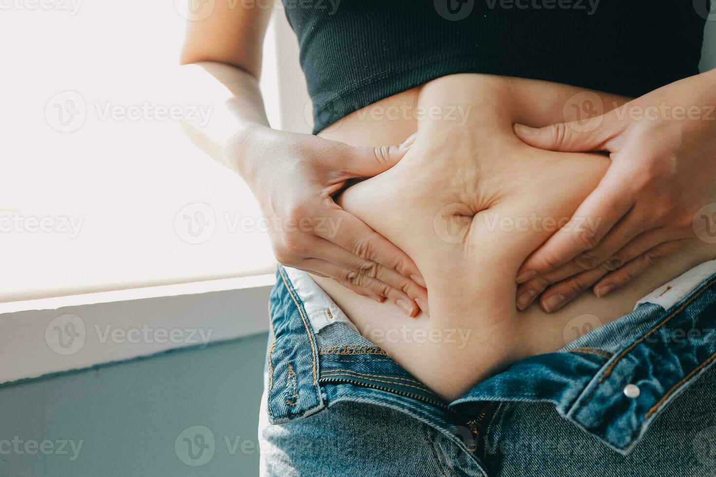 Close up of a belly with scar from c-section and abdominal fat. Women's health. A woman dressed up in sportswear demonstrating her imperfect body after a childbirth with nursery on the background. photo