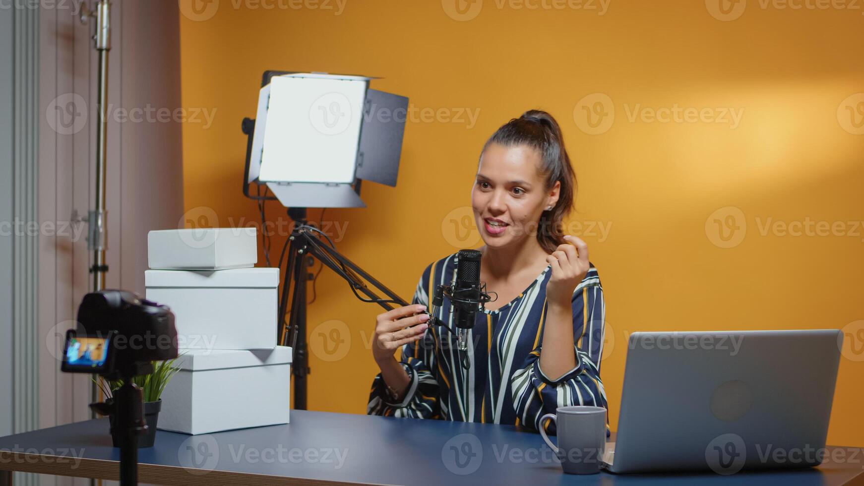 Influencer talking to camera and giveaway boxes are on the desk ready for loyal subscribers. Creative content creator social media star expert vlogger recording online internet web podcast gift for audience photo