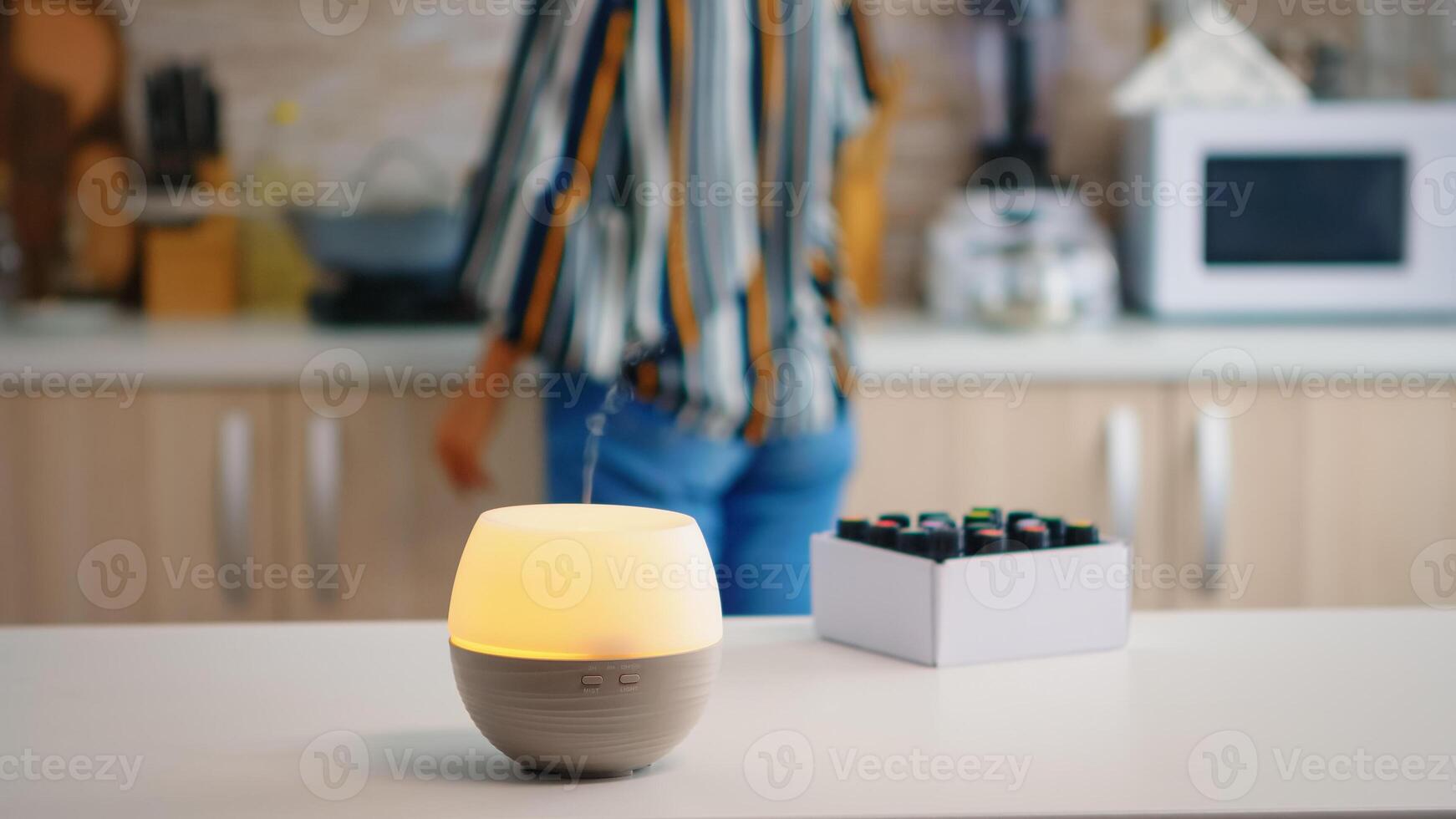 Woman in the kitchen with essential oils diffuser working on the table top. Aroma health essence, welness aromatherapy home spa fragrance tranquil theraphy, therapeutic steam, mental health treatment photo