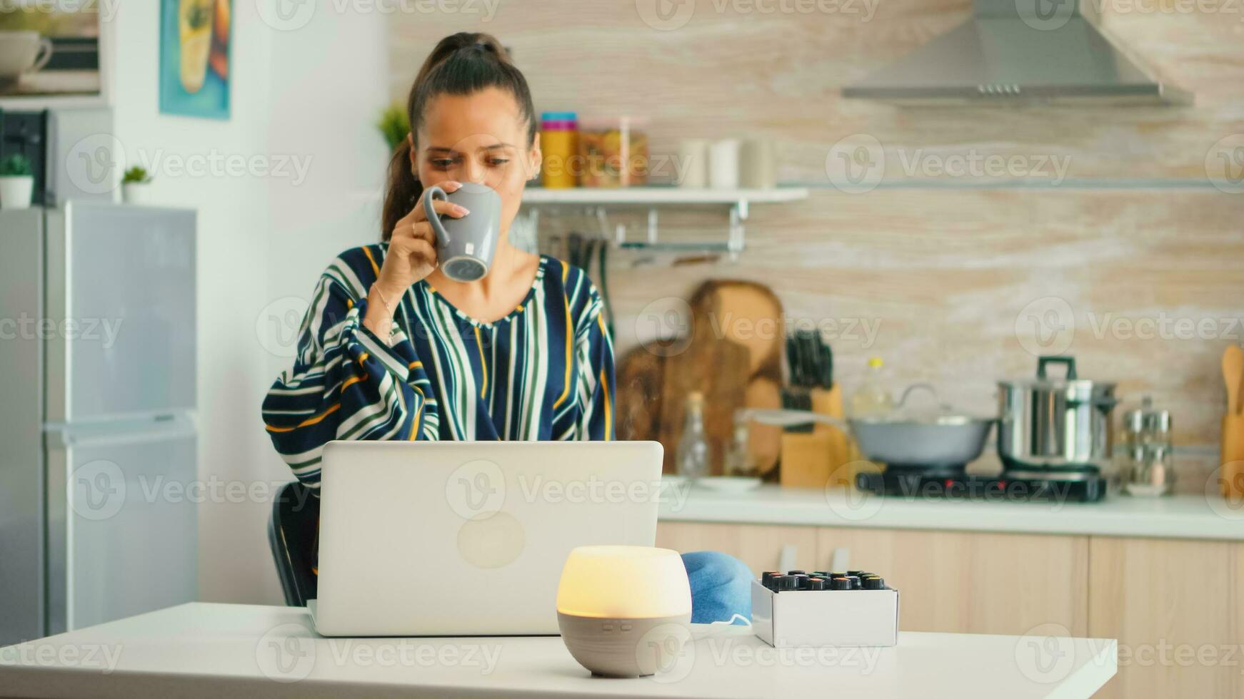 Drinking coffe and working with aromather apy essential oils diffuser in the kitchen. Aroma health essence, welness aromatherapy home spa fragrance tranquil theraphy, therapeutic steam, mental health treatment photo