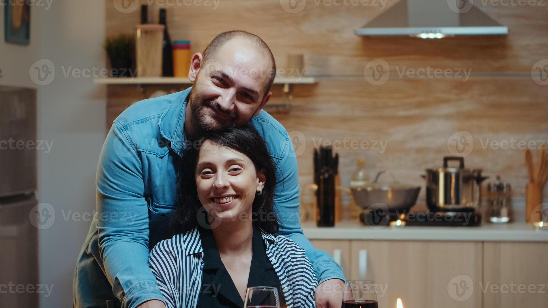 Portret of cheerful couple looking at camera, smiling, sitting at table in kitchen during romantic dinner. Happy married poeple special tender moments, enjoyng the meal at candle lights celebration photo