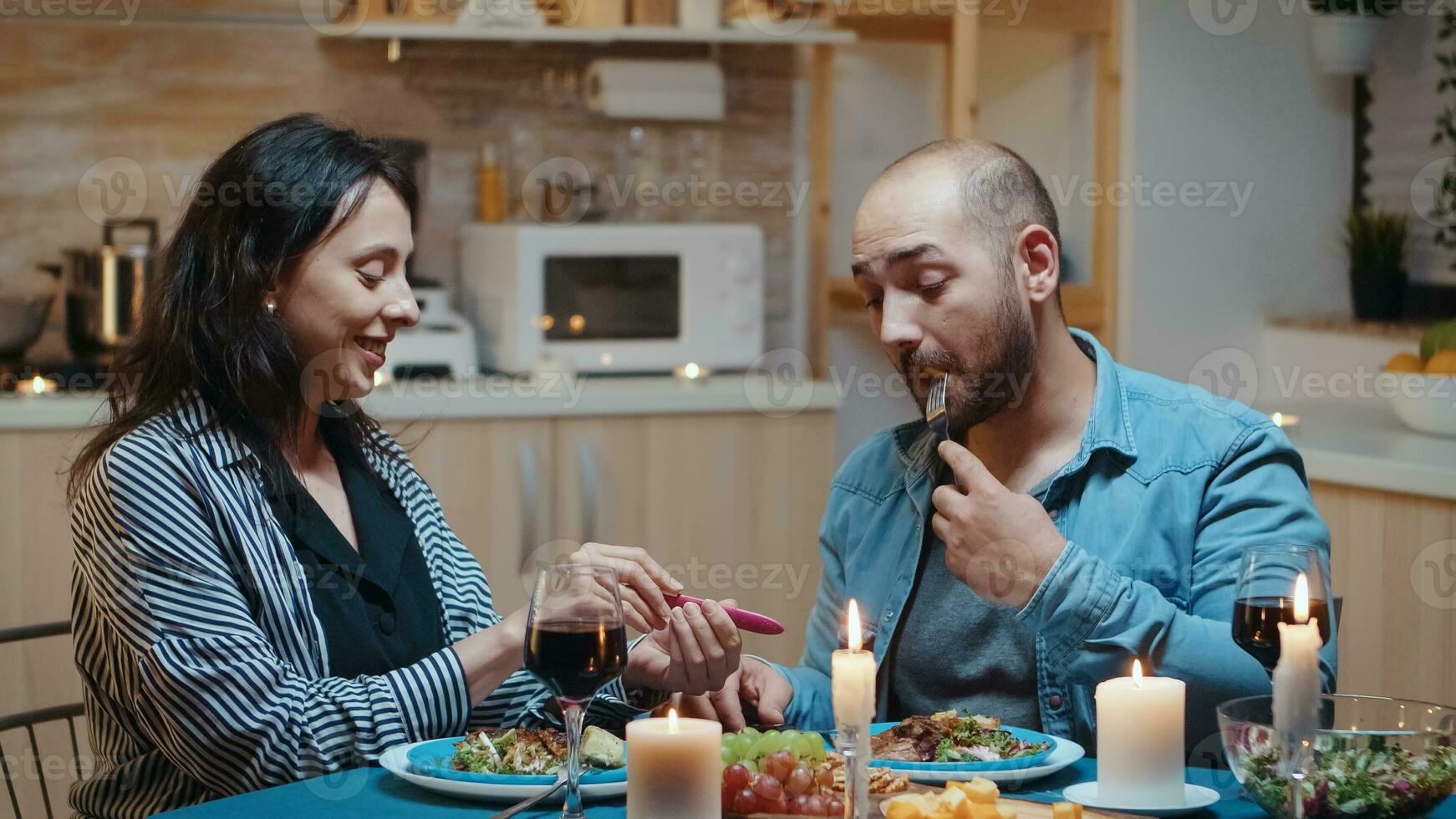 Happy young couple with pregnancy news during romantic dinner, sitting in the kitchen. Excited couple smiling, hugging and kissing each other for positive results. Pregnant wife embracing man. photo