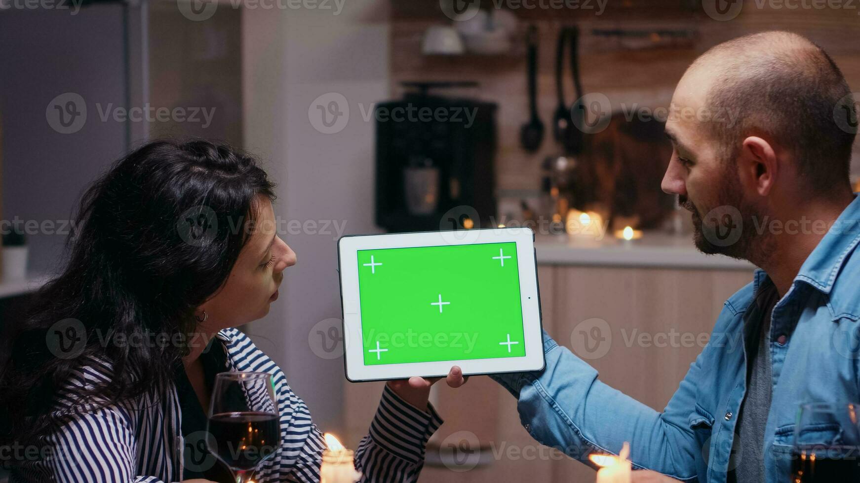 joven caucásico Pareja utilizando verde Bosquejo pantalla digital aislado tableta computadora. marido y esposa mirando a verde pantalla modelo croma llave monitor sentado a el mesa en cocina durante cena. foto