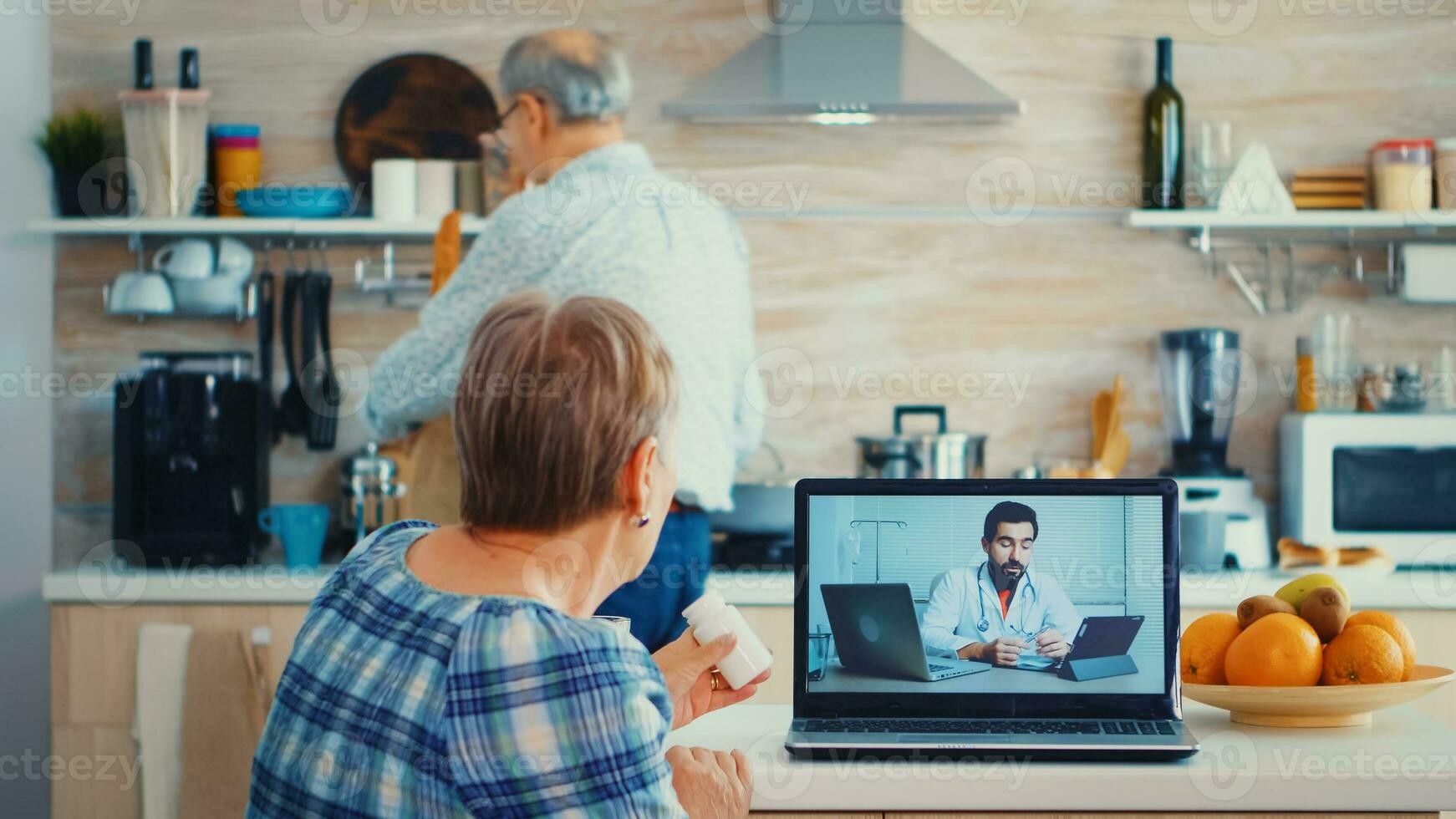Senior woman holding bottle of pills during video conference with doctor using laptop in kitchen. Online health consultation for elderly people drugs ilness advice on symptoms, physician telemedicine webcam. Medical care internet chat photo