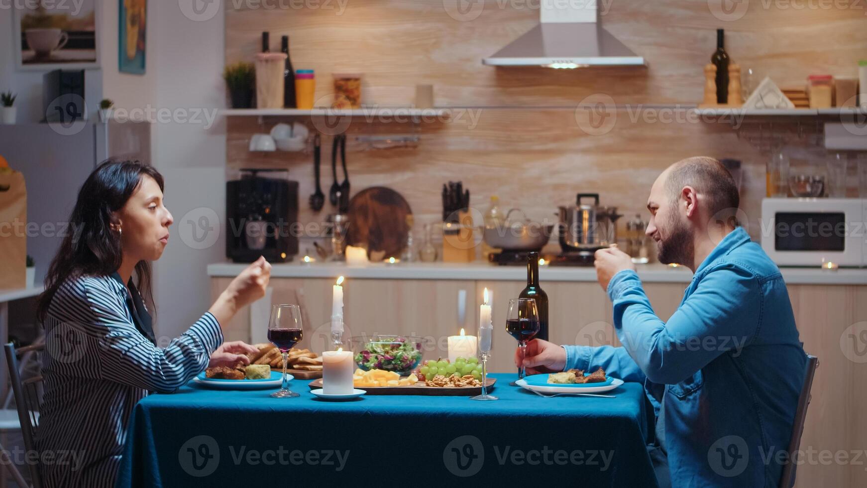Caucasian young couple having romantic dinner in the kitchen after job. Happy people talking, sitting at table in dining room, enjoying the meal, celebrating their anniversary at home with healty food photo