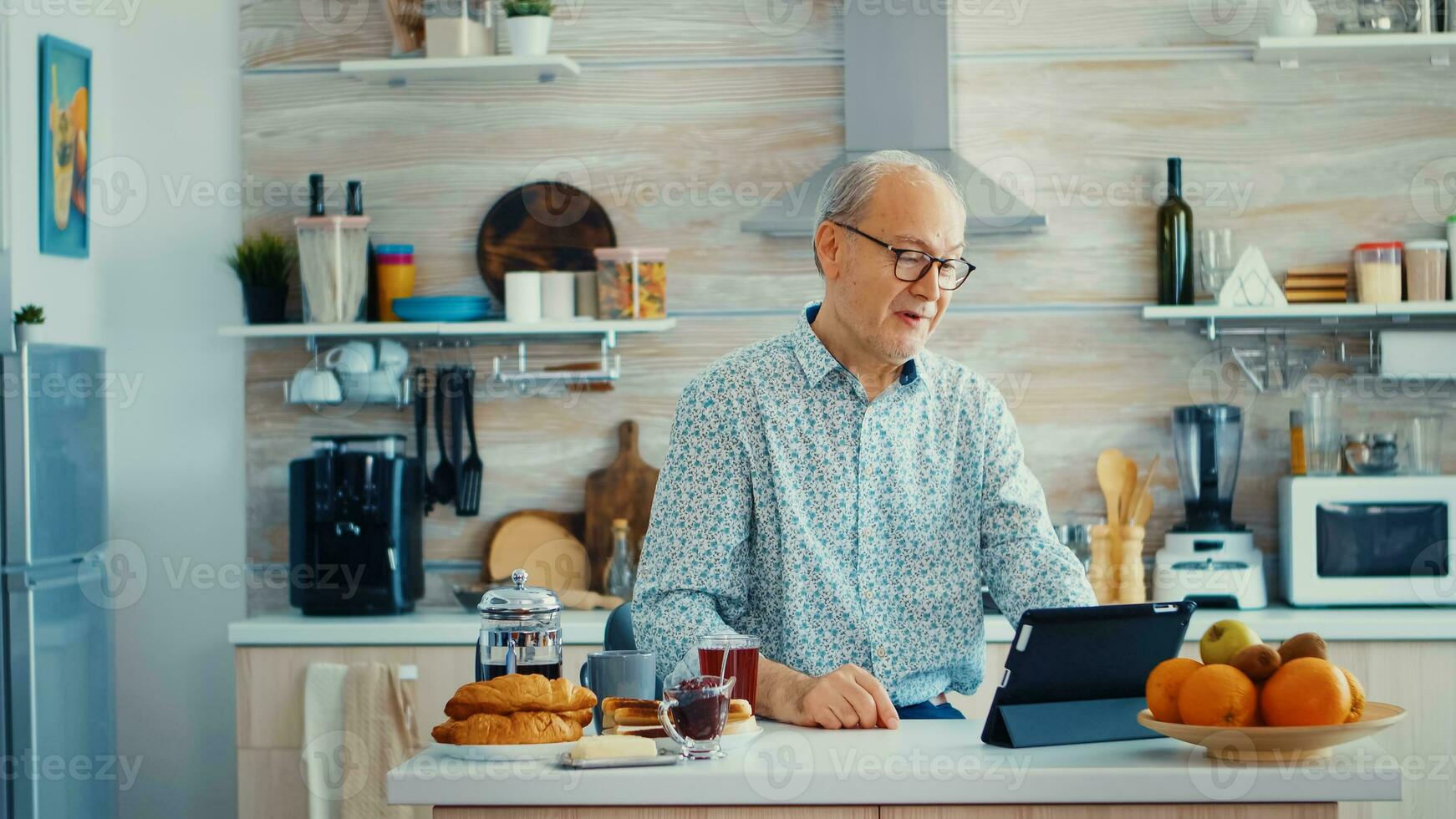 Happy senior man during breakfast in kitchen having a video conference with family. Elderly person using internet online chat technology video webcam making a video call connection camera communication conference call photo