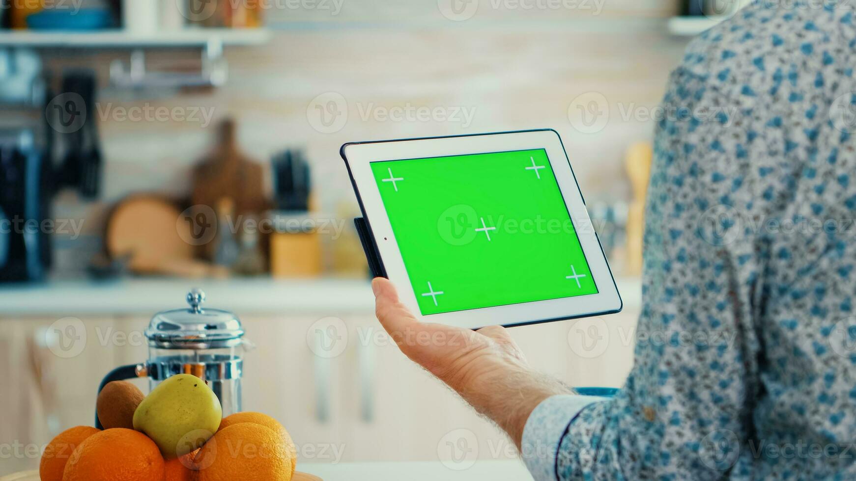 Mature man holding tablet pc with chroma key in kitchen during breakfast. Elderly person with green screen isolated mockup mockup for easy replacement photo