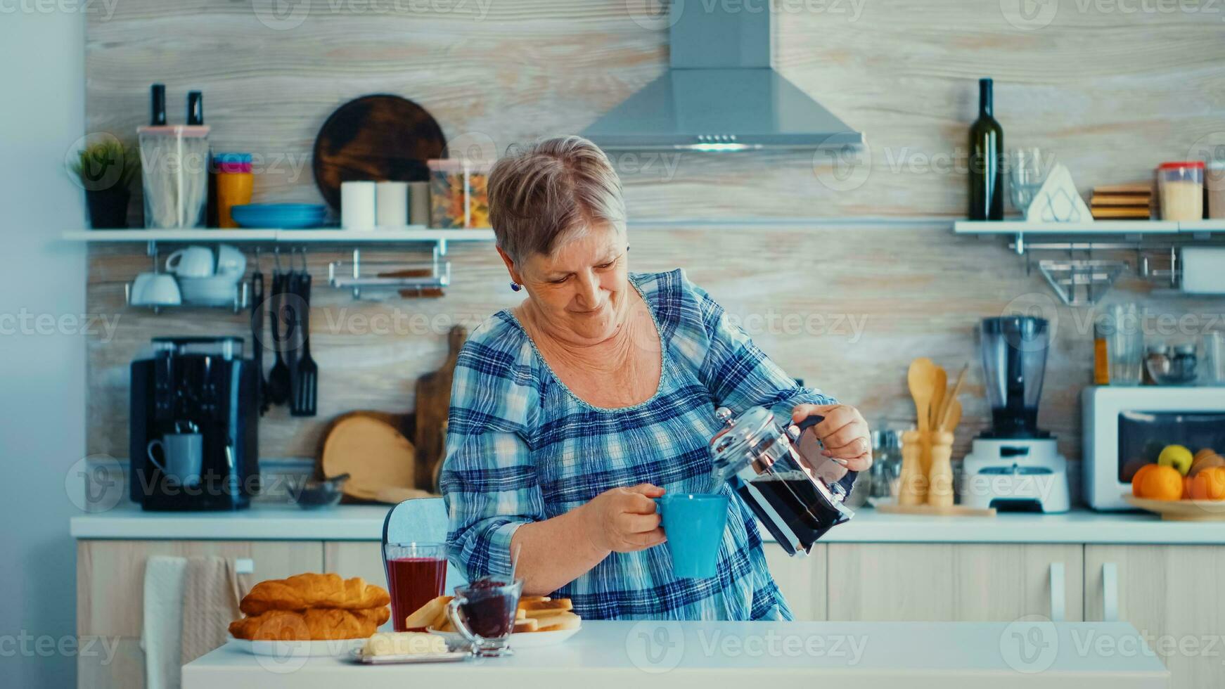 Mature woman using french press to make coffee in kitchen during breakfast. Elderly person in the morning enjoying fresh brown cafe espresso cup caffeine from vintage mug, filter relax refreshment photo