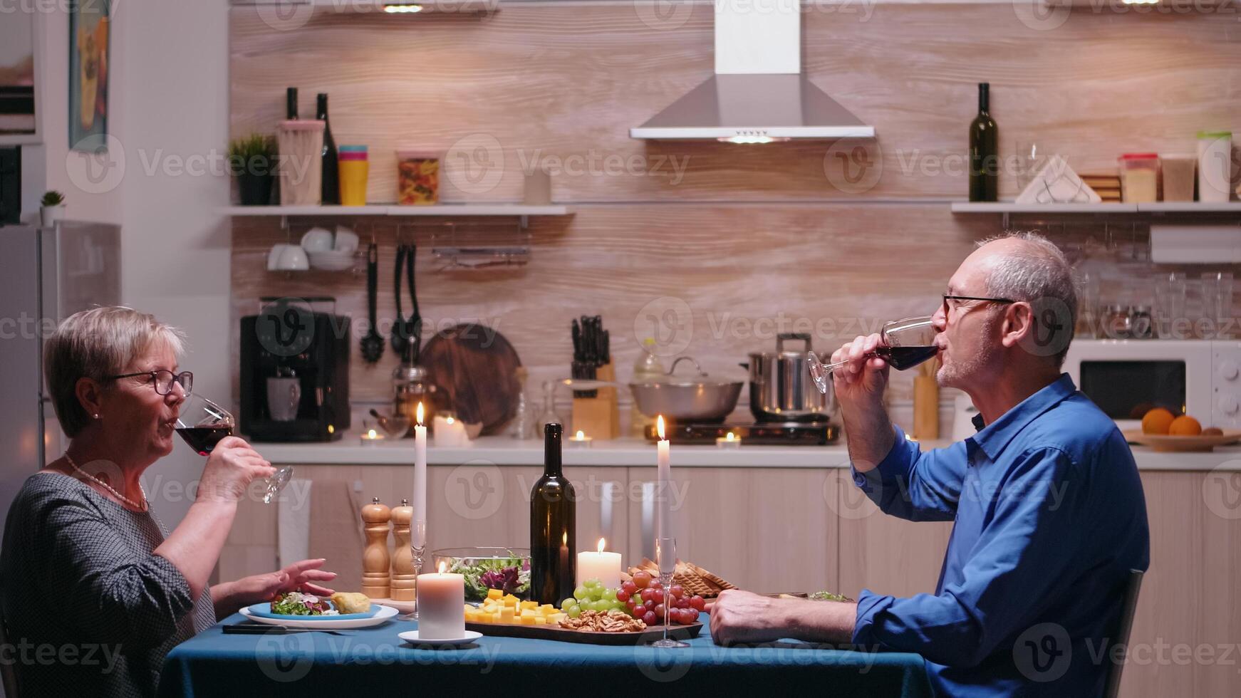 Loving mature couple raising champagne glass and toasting while enjoying romantic dinner at home in the kitchen. Senior old people eating the meal, celebrating their anniversary in the dining room. photo