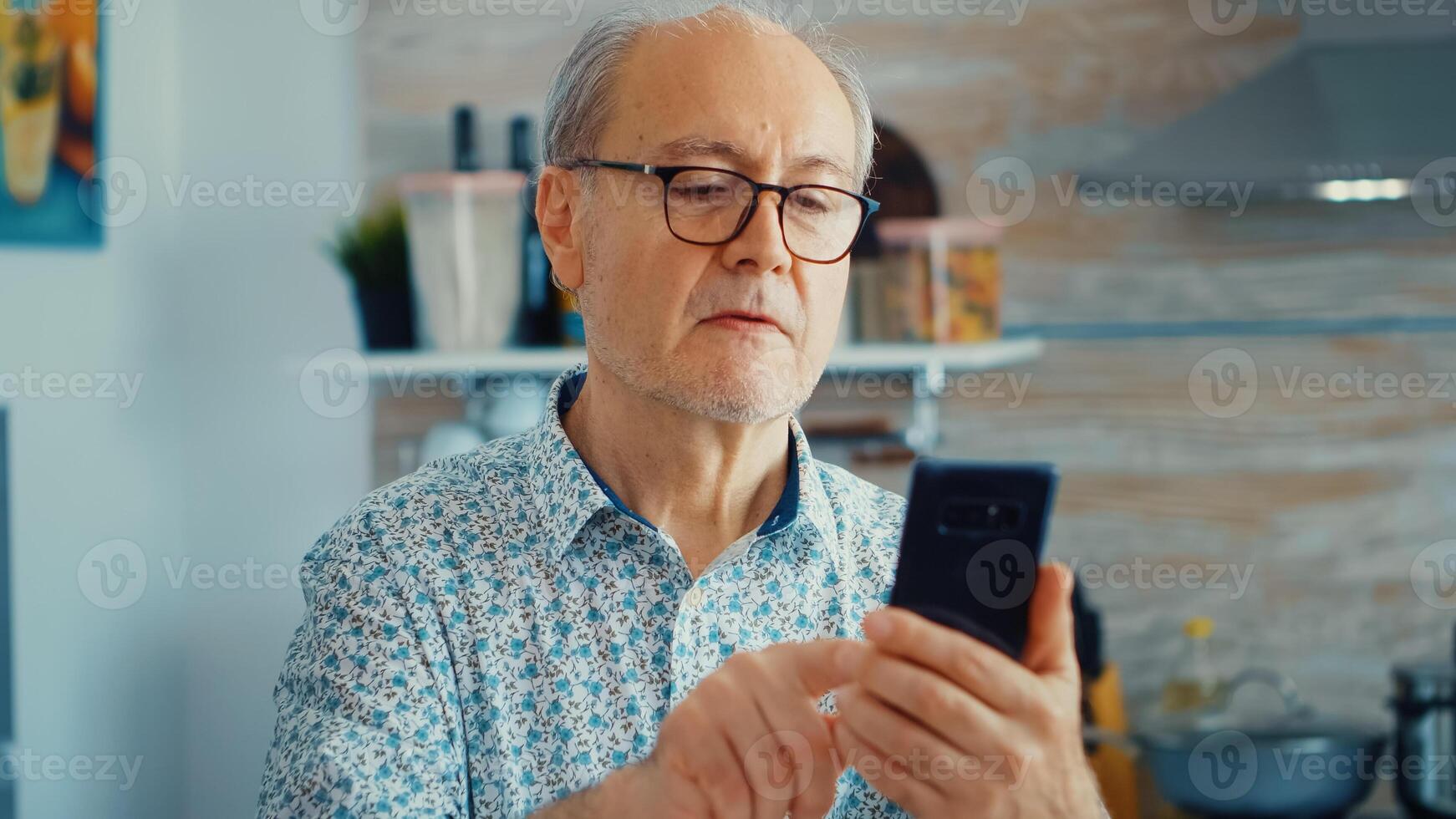 Old man surfing on social media using smartphone during breakfast in kitchen. Authentic portrait of retired senior enjoying modern internet online technology photo