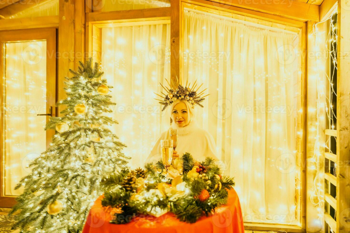 Happy smiling woman in a white dress holding a champagne glass in front of a Christmas tree. photo