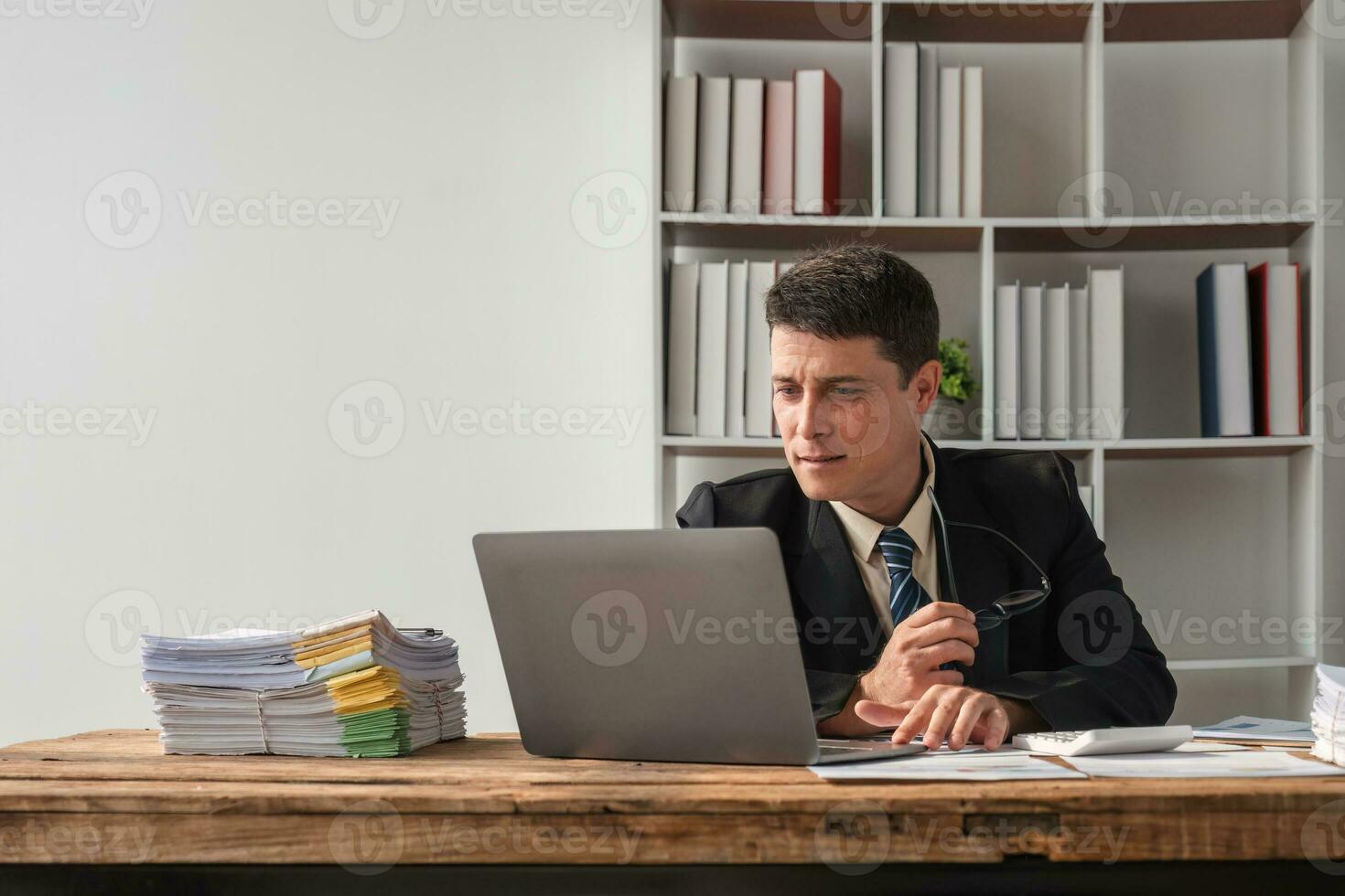Unhappy young businessman feeling bored and stressed at work looking at laptop with hopeless expression while sitting in office photo
