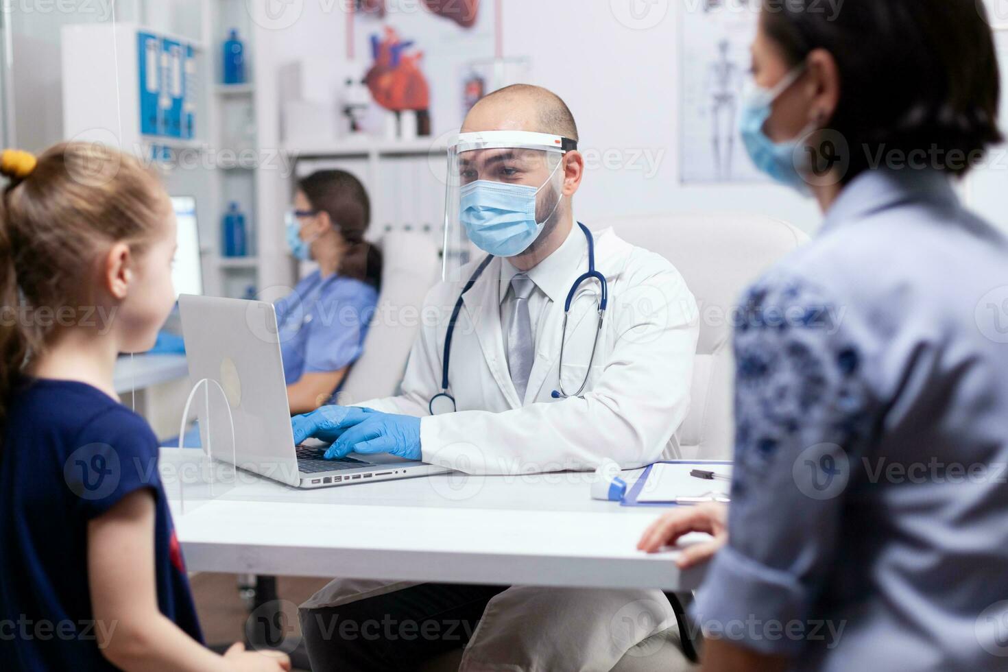 Doctor consulting child patient sitting next to her mother during coronavirus pandemic and wearing face mask. Specialist in medicine providing health care services examination, radiographic treatment in clinic. photo