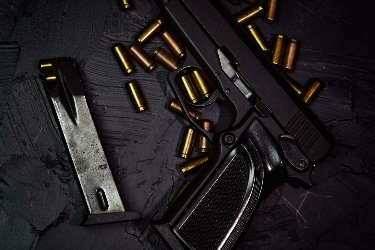 Flat lay of gun and cartridge with bullets. Weapons on concrete table. Pistol for defense or attack. Concept of crime ammunition and physical evidence. Firearms on dark background. photo