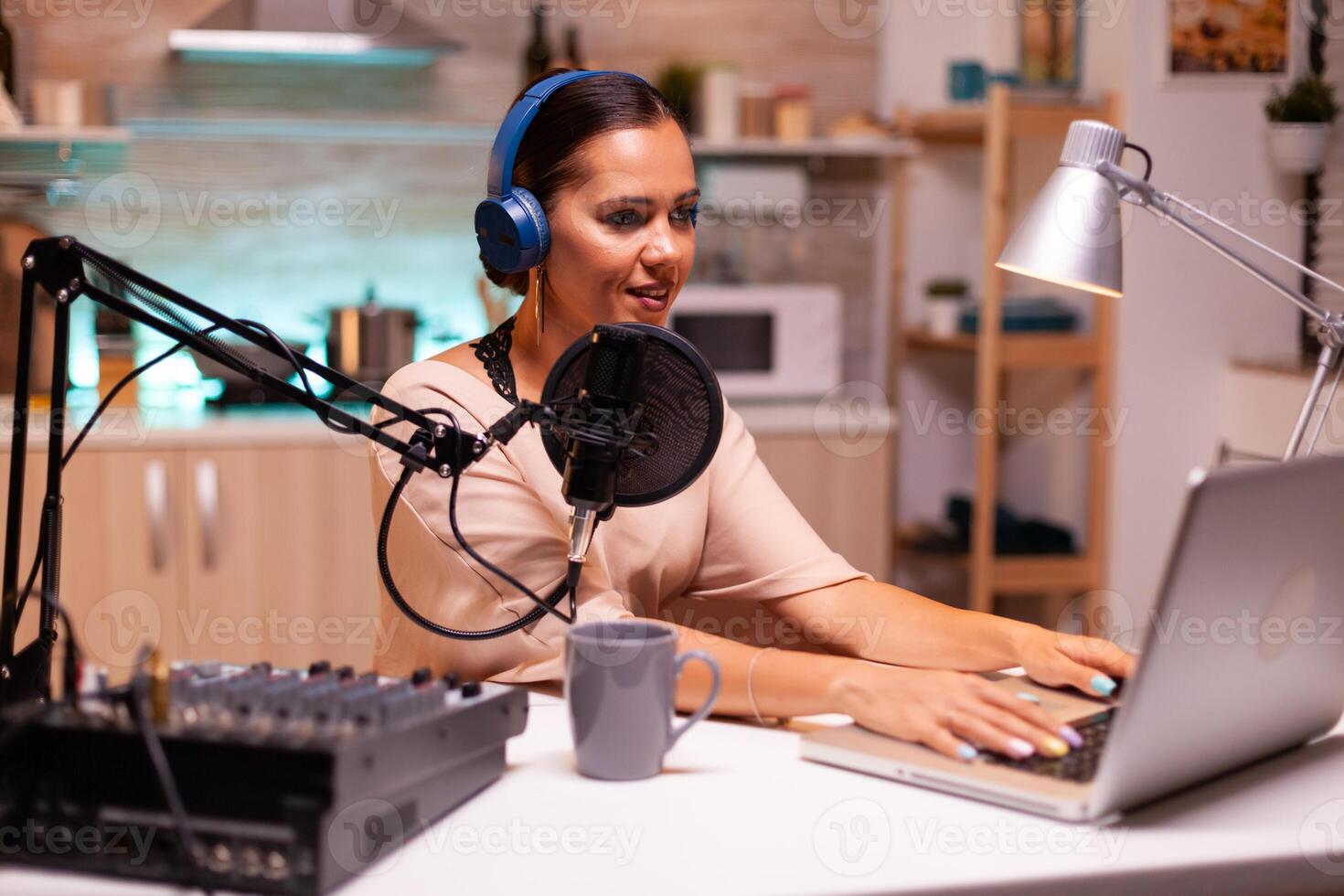 Video blogger typing on laptop and recording voice for podcast using professional microphone. Creative online show On-air production internet broadcast show host streaming live content. photo