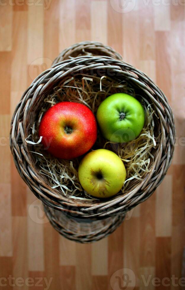 Whole Variety Colored Ripe Apples In A Wood Shavings Inside A Wicker Basket On A Wooden Planks Background photo