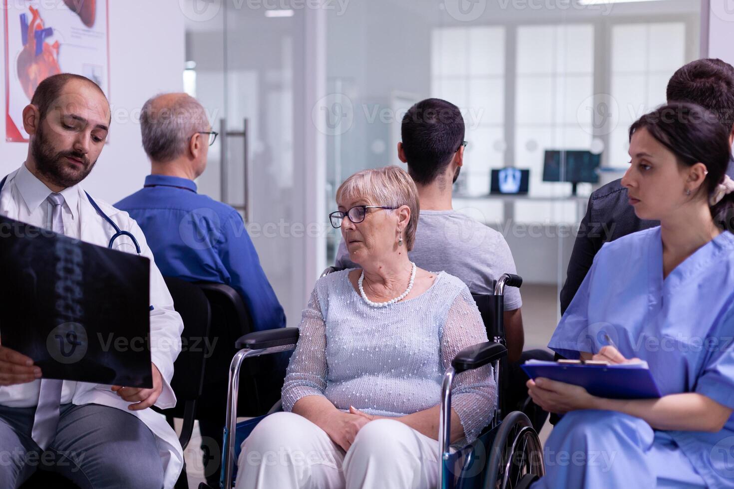 Doctor with stethoscope communicating to disabled senior woman radiography in wheelchair test result while sitting in hospital waiting area. Disabled elderly patient waiting for medical examination photo
