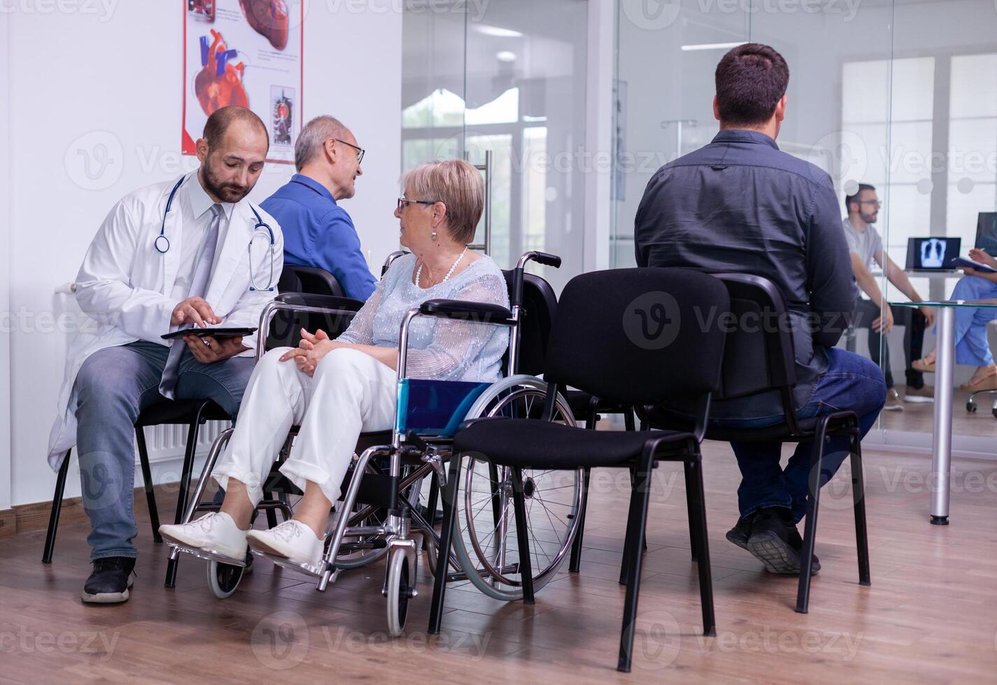 Hospital doctor in white coat communicating to senior woman in wheelchair x-ray radiography using tablet computer. Medic specialist explanining illness treatment while sitting on chair in waiting area photo