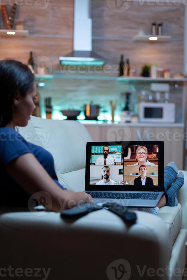 Woman freelancer having web chat conference sitting on sofa in living room. Remote worker discussing at online meeting, consulting with colleagues using videocall and webcam working in front of laptop photo