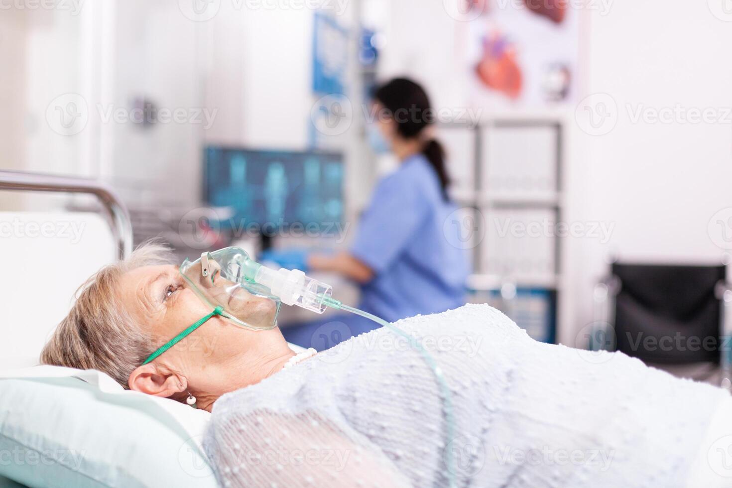 Elderly woman having respiratory disease because of covid19 with oxygen mask. Patient in hospital room laying on medical bed with infected lung during coronavirus pandemic having respiratory problem. photo