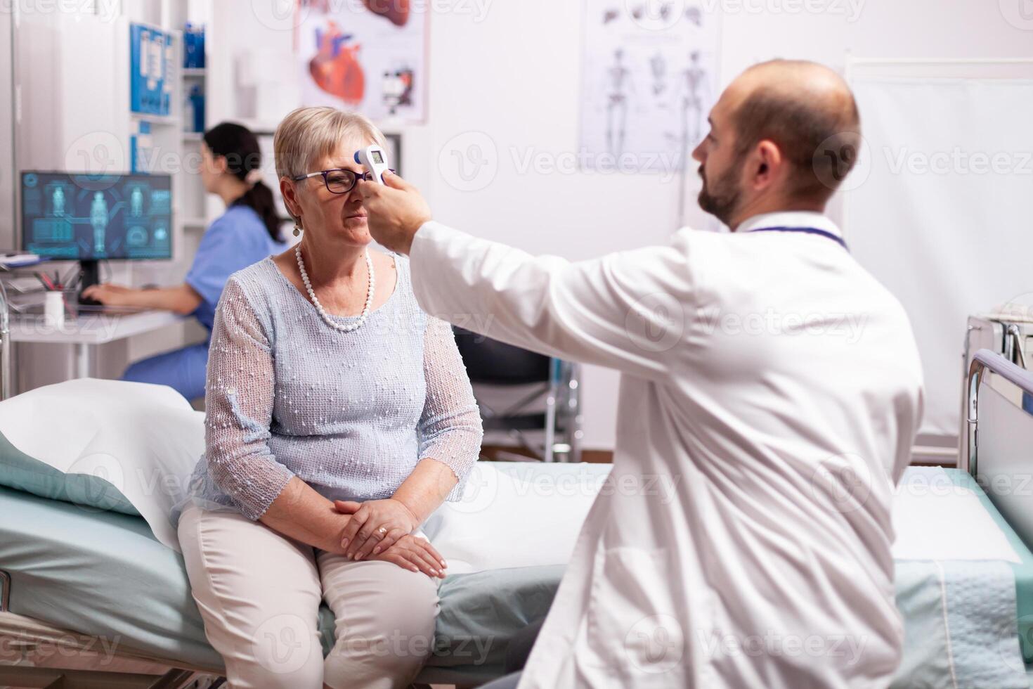 Worried doctor taking body temperature of senior woman during consultation sitting on hospital bed. Medical consultation for infections and disease during global pandemic,flu, tool, sickness. photo
